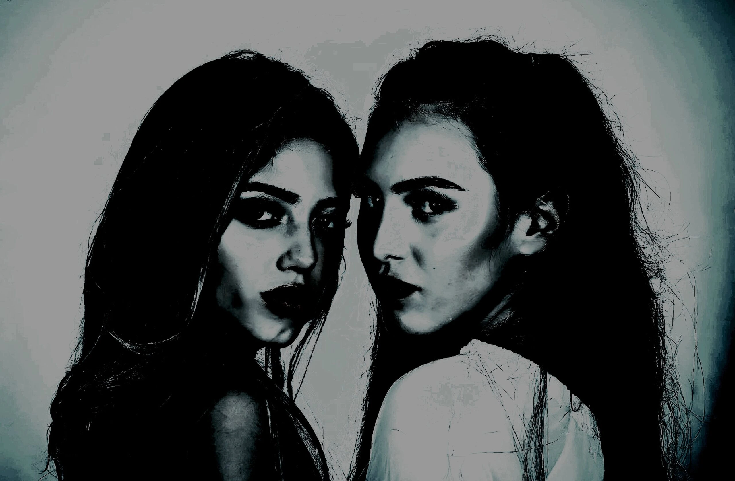 Two women with intense expressions in dark, moody lighting, gazing directly at the camera.