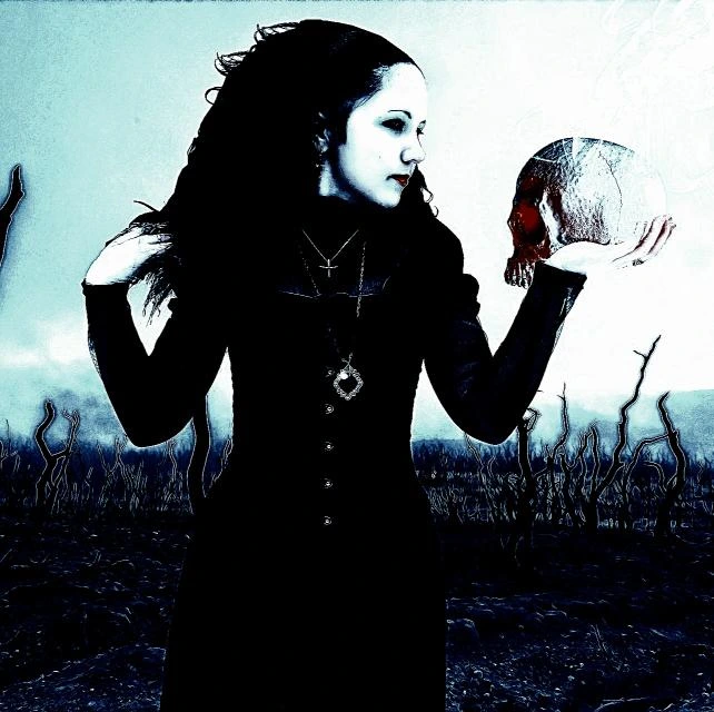 Gothic woman in a black dress holding a skull in a dark, surreal outdoor setting.

