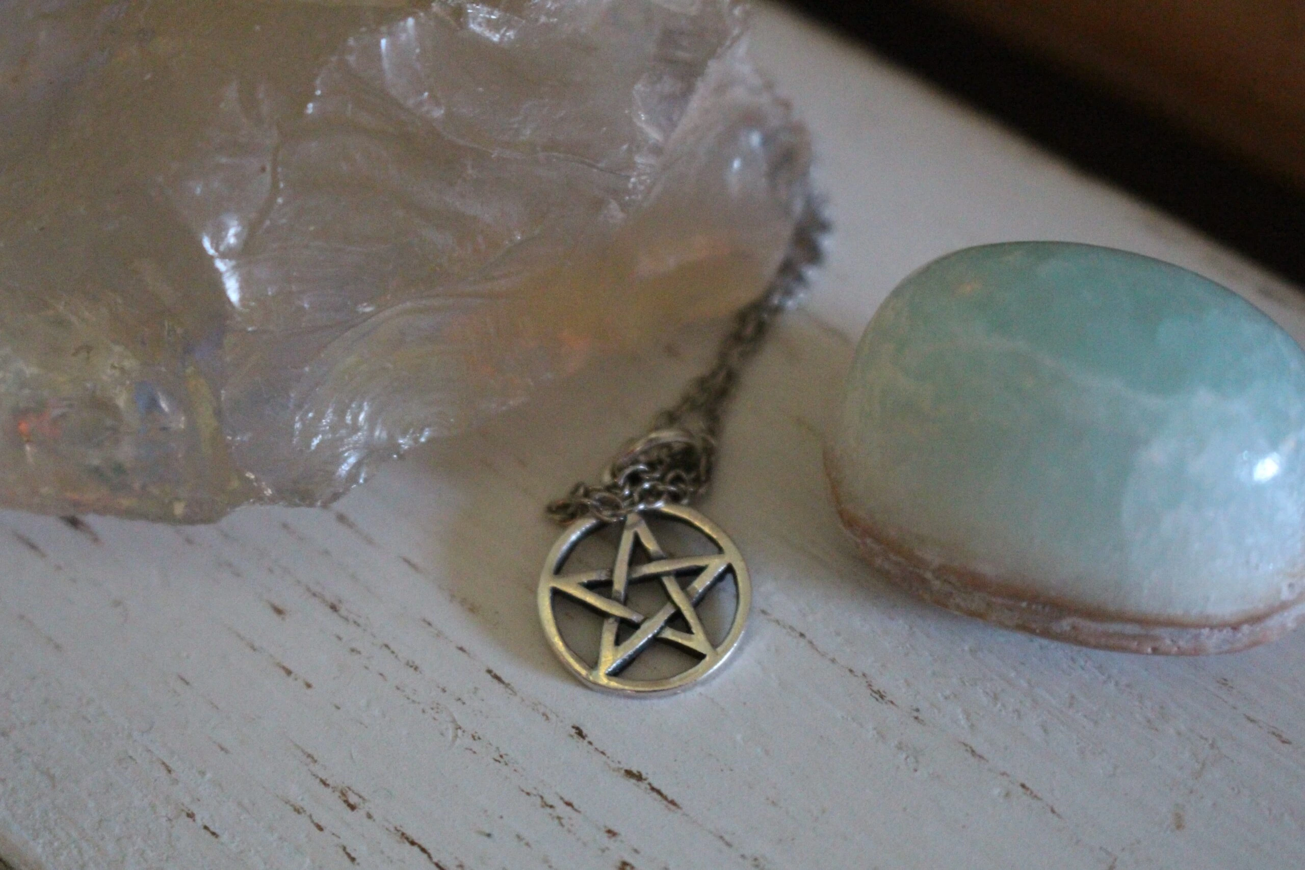 Pentagram necklace resting on a wooden surface with crystals, emphasizing gothic and mystical symbolism.