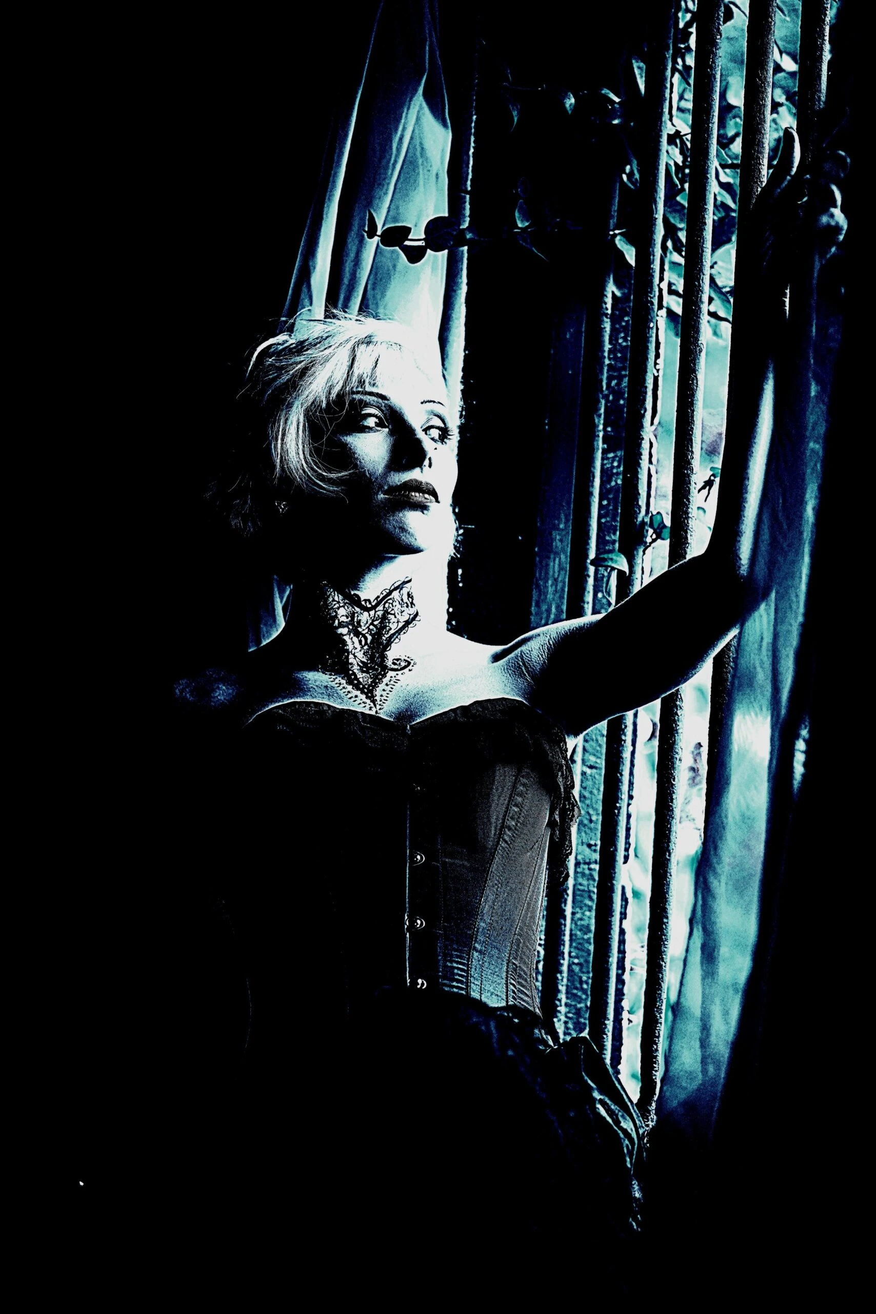 Dramatic portrait of a woman in a corset gazing through a window with eerie lighting.