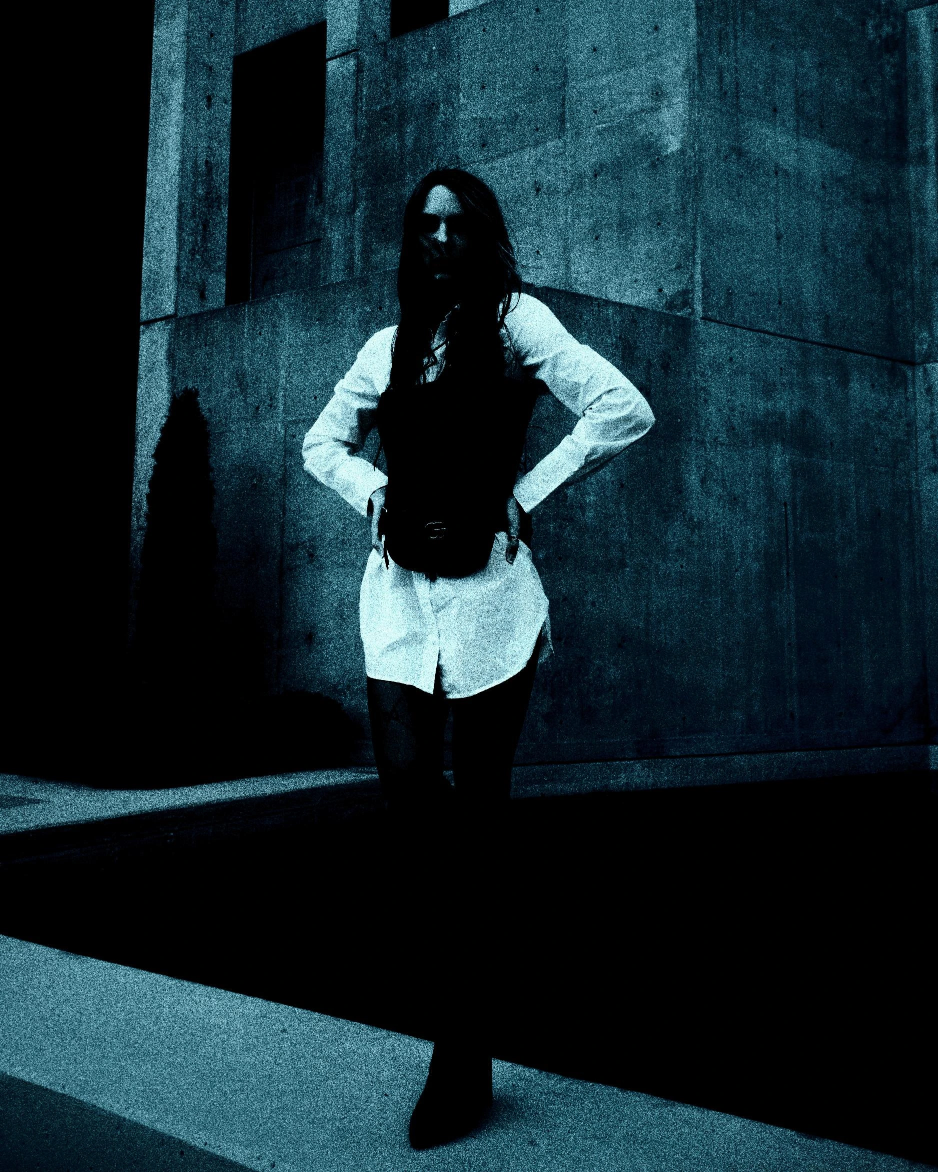 Woman in a white shirt and corset posing confidently in front of a modern concrete building.