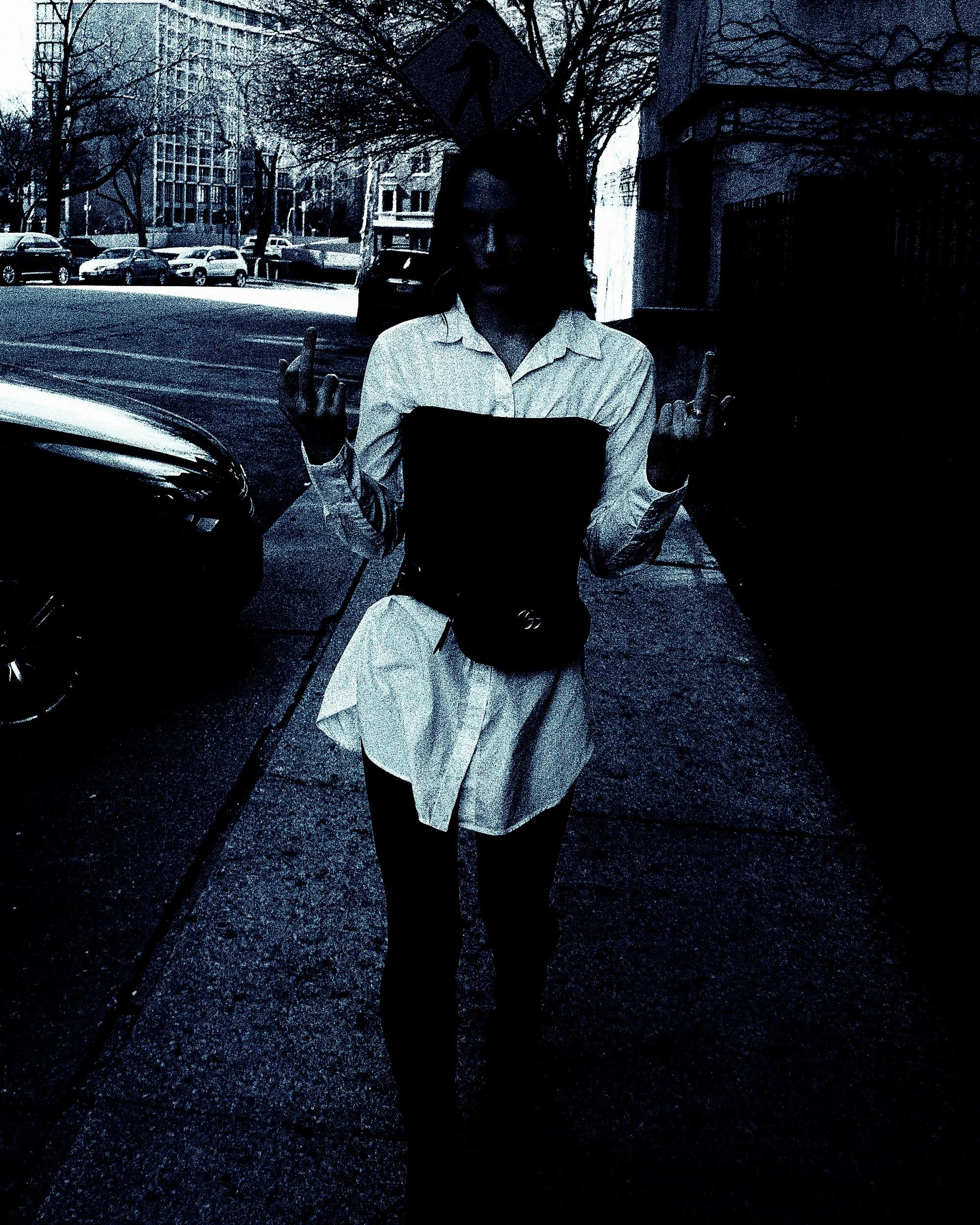 Street photo of a woman in a corset and white shirt giving a rebellious gesture while walking.