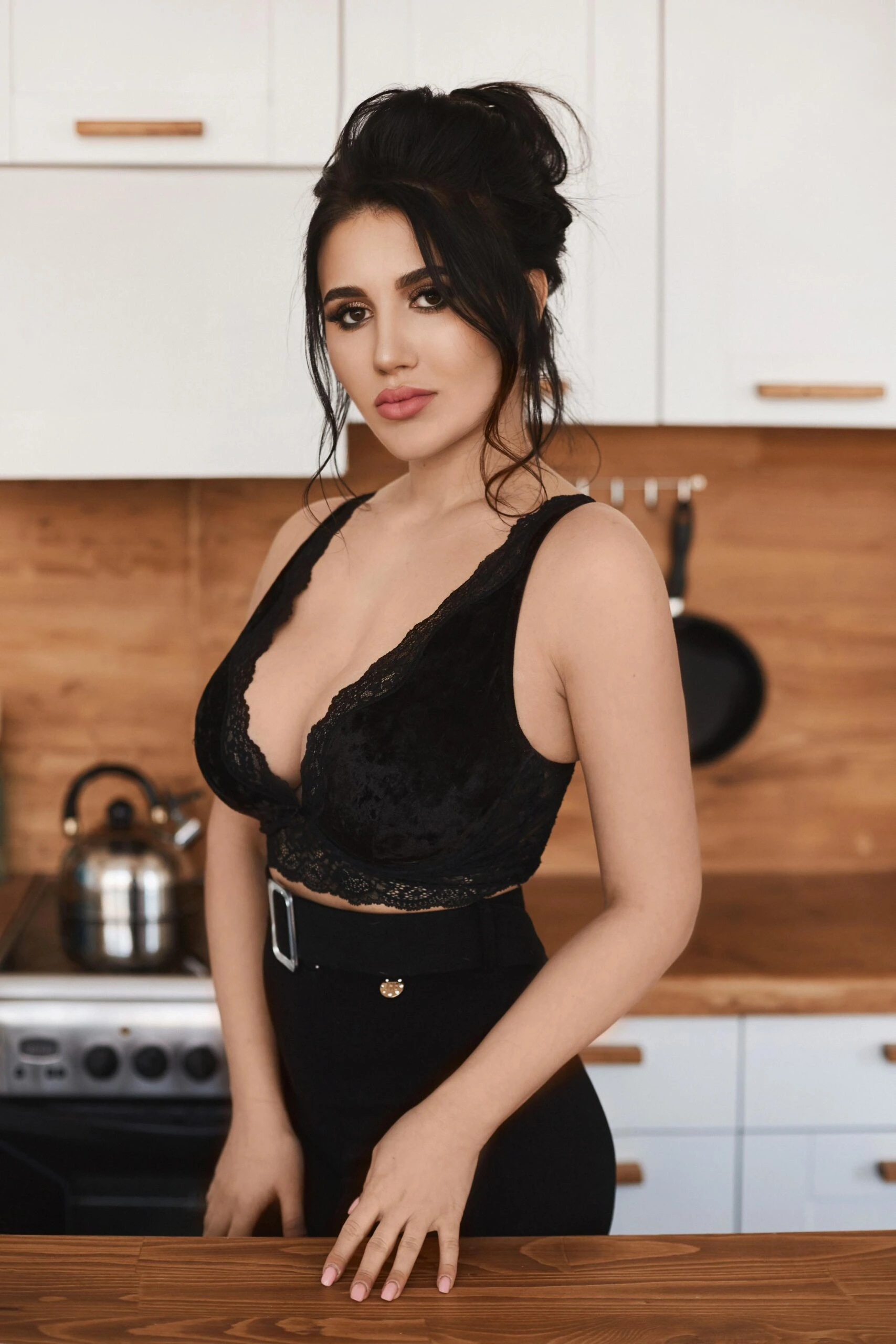 Woman with dark hair in a black lace top standing confidently in a modern kitchen.