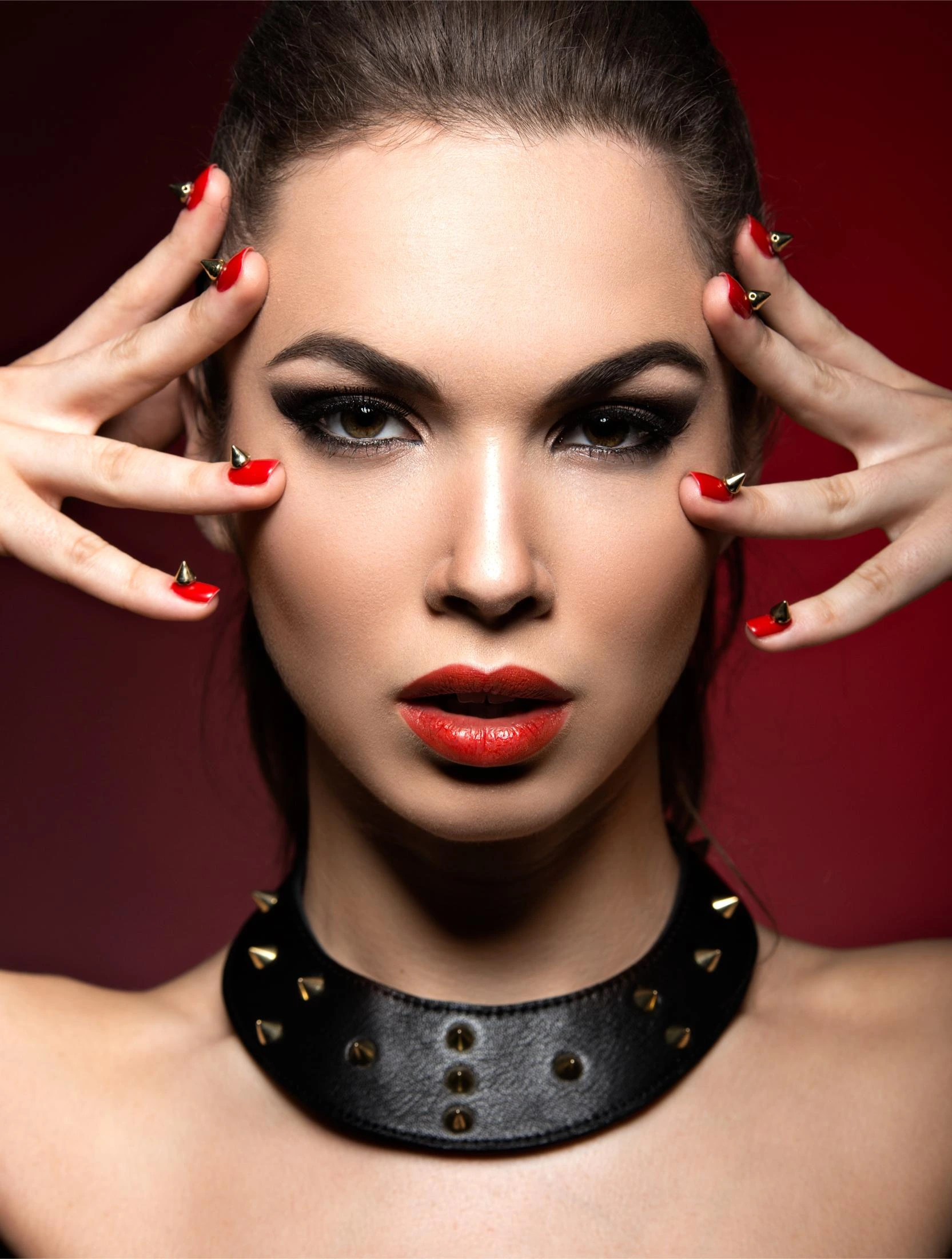 A striking woman wearing a studded leather choker with bold red lipstick and spiked nail designs, embodying edgy gothic fashion.