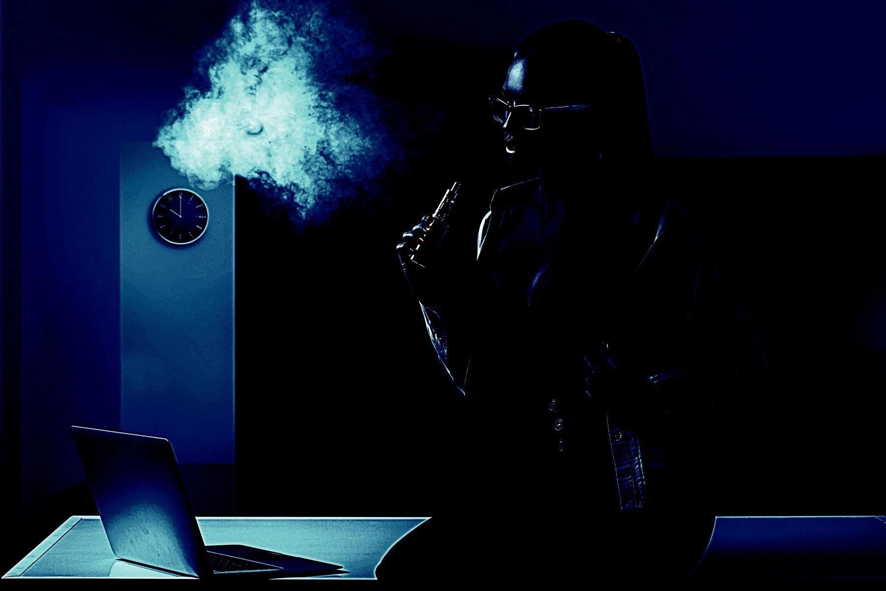 Silhouette of a woman vaping indoors, with smoke illuminated in blue light and a laptop on the table.