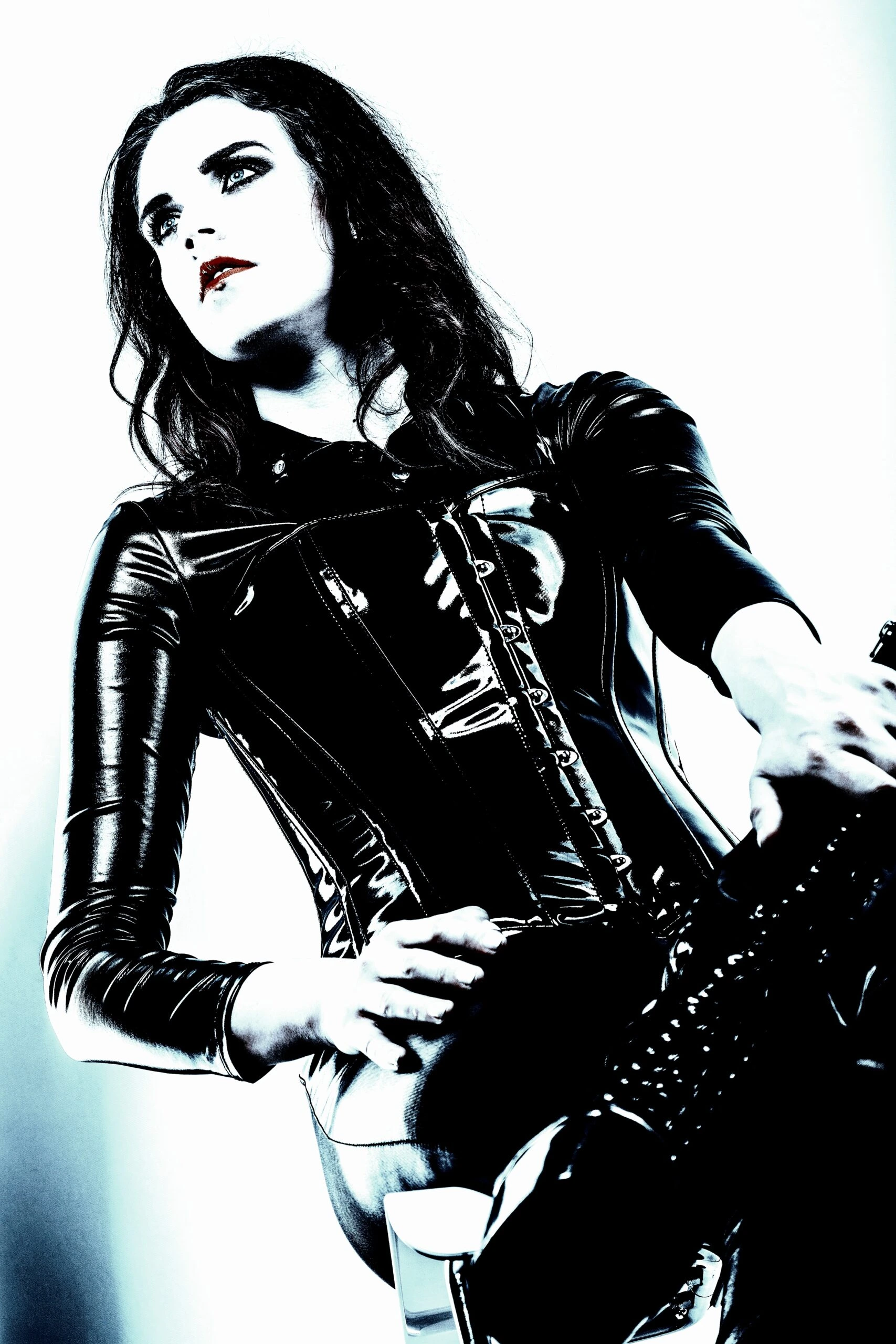 A woman wearing a tight black latex corset stands confidently, her piercing gaze and dark makeup embodying a powerful, gothic aesthetic.