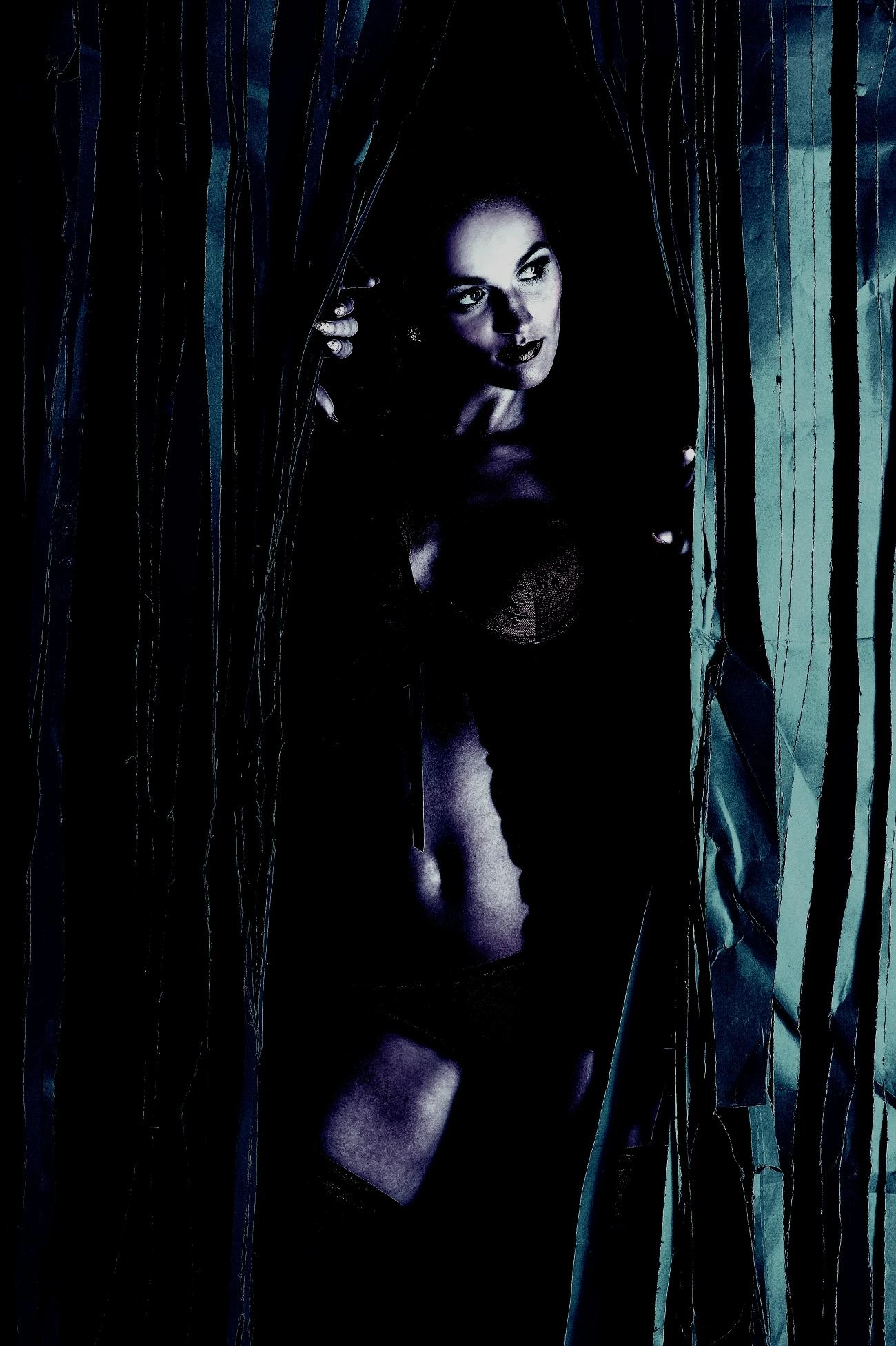 Artistic shot of a woman in gothic lingerie, surrounded by dark drapes with dramatic lighting creating a mysterious ambiance.
