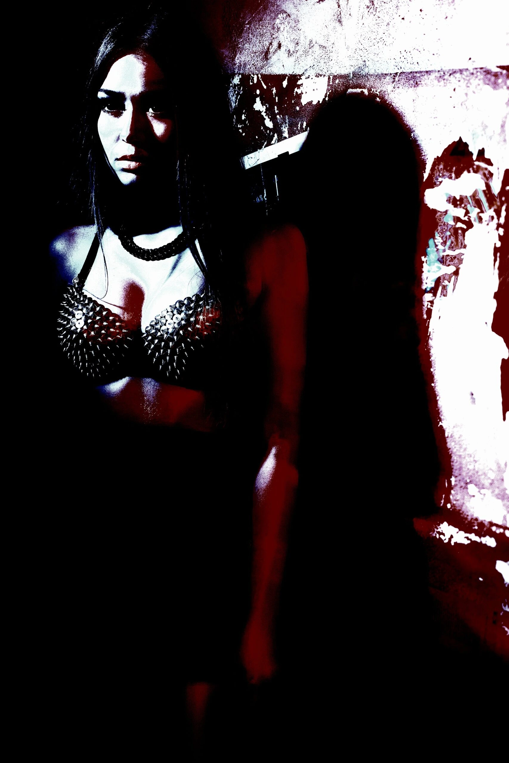 A woman in a spiked bra top stands against a distressed wall, her intense expression and shadows highlighting a rebellious, alternative style.