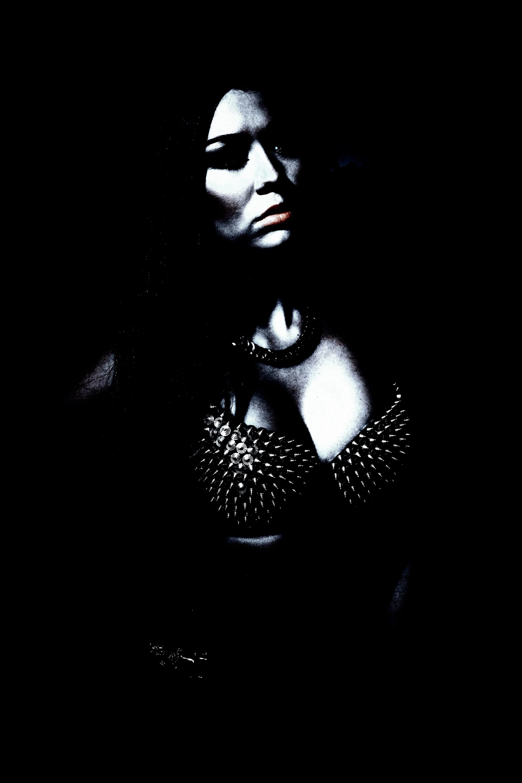 A mysterious woman in a dark environment, her face and spiked bra partially illuminated, creating a striking contrast of light and shadow.