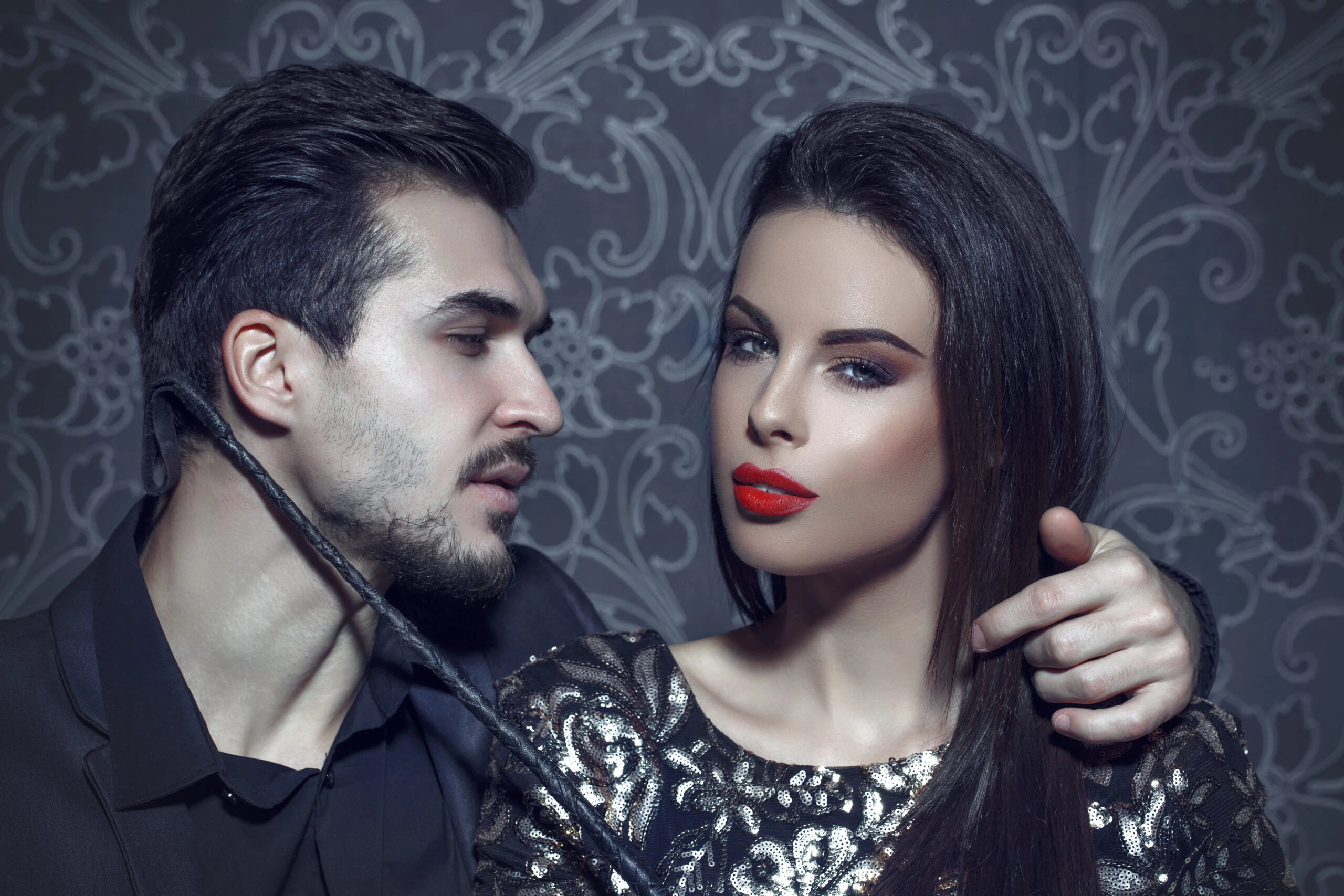 Man holding a leather whip near a woman's neck, capturing a subtle exchange of power and control.