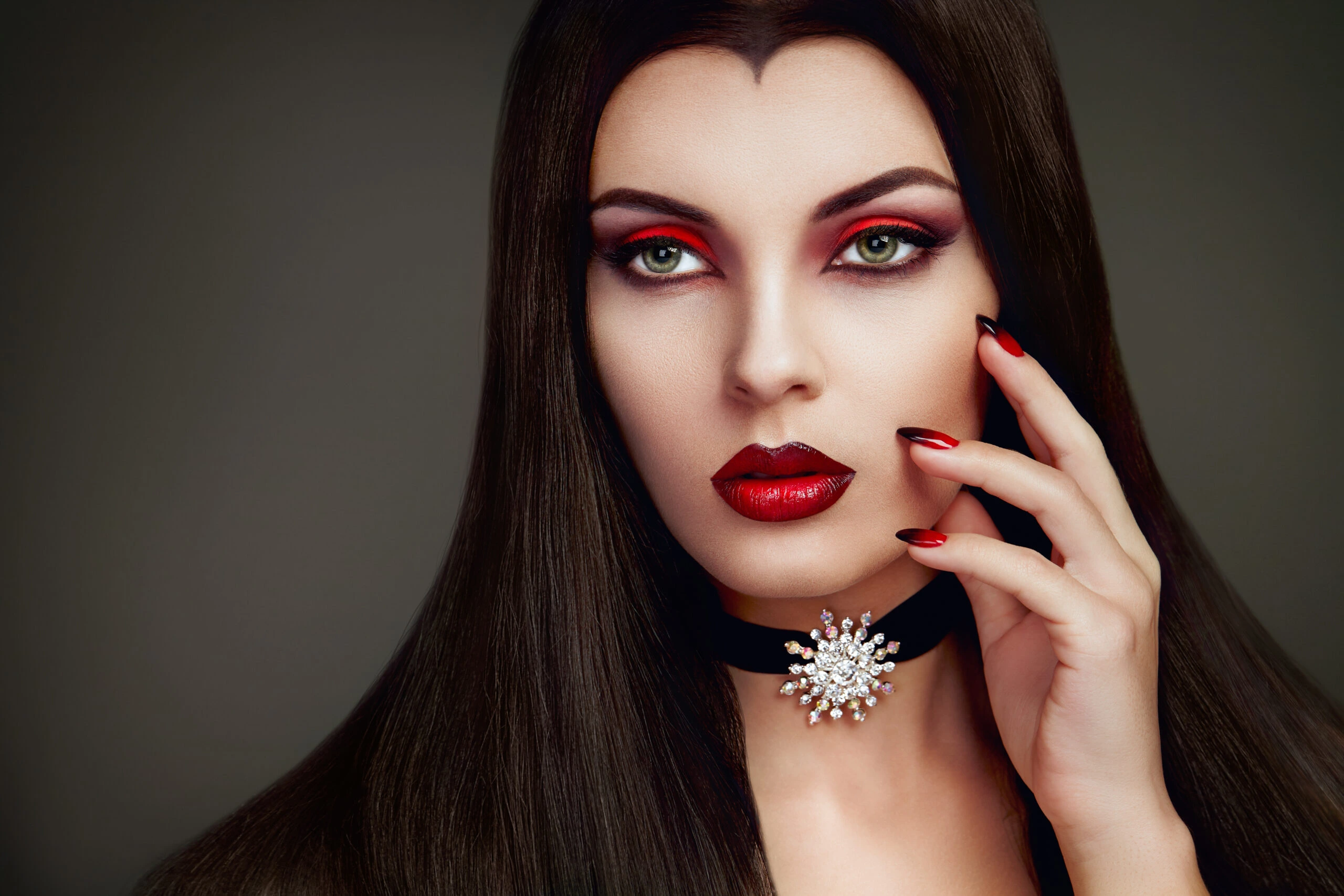 Glamorous woman with long dark hair and red lips, wearing a black choker with a sparkling gem brooch, embodying a vampiric style.