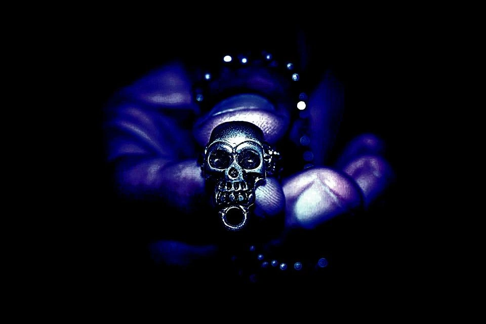Close-up of a gothic skull pendant held in a hand with a dark, moody background.