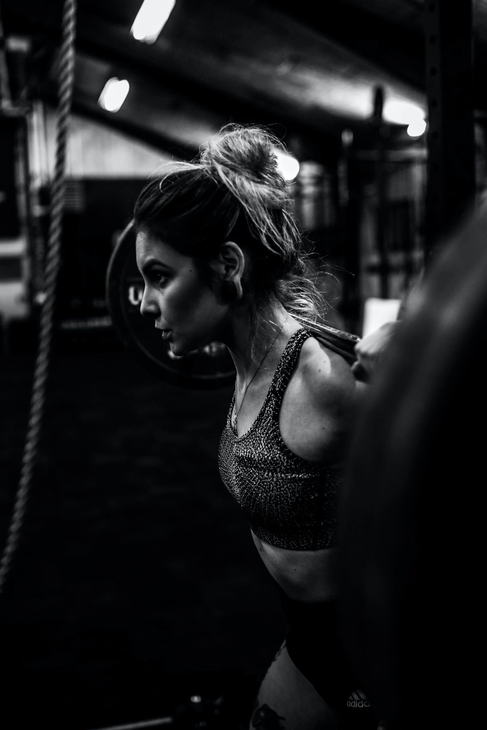 Woman lifting a barbell in a dark gym, focused and determined during her strength training session.