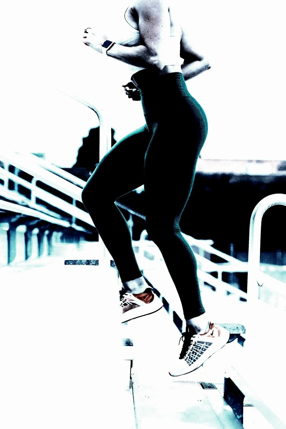 Woman running up stairs outdoors, wearing sleek athletic leggings and trainers, framed by soft lighting.
