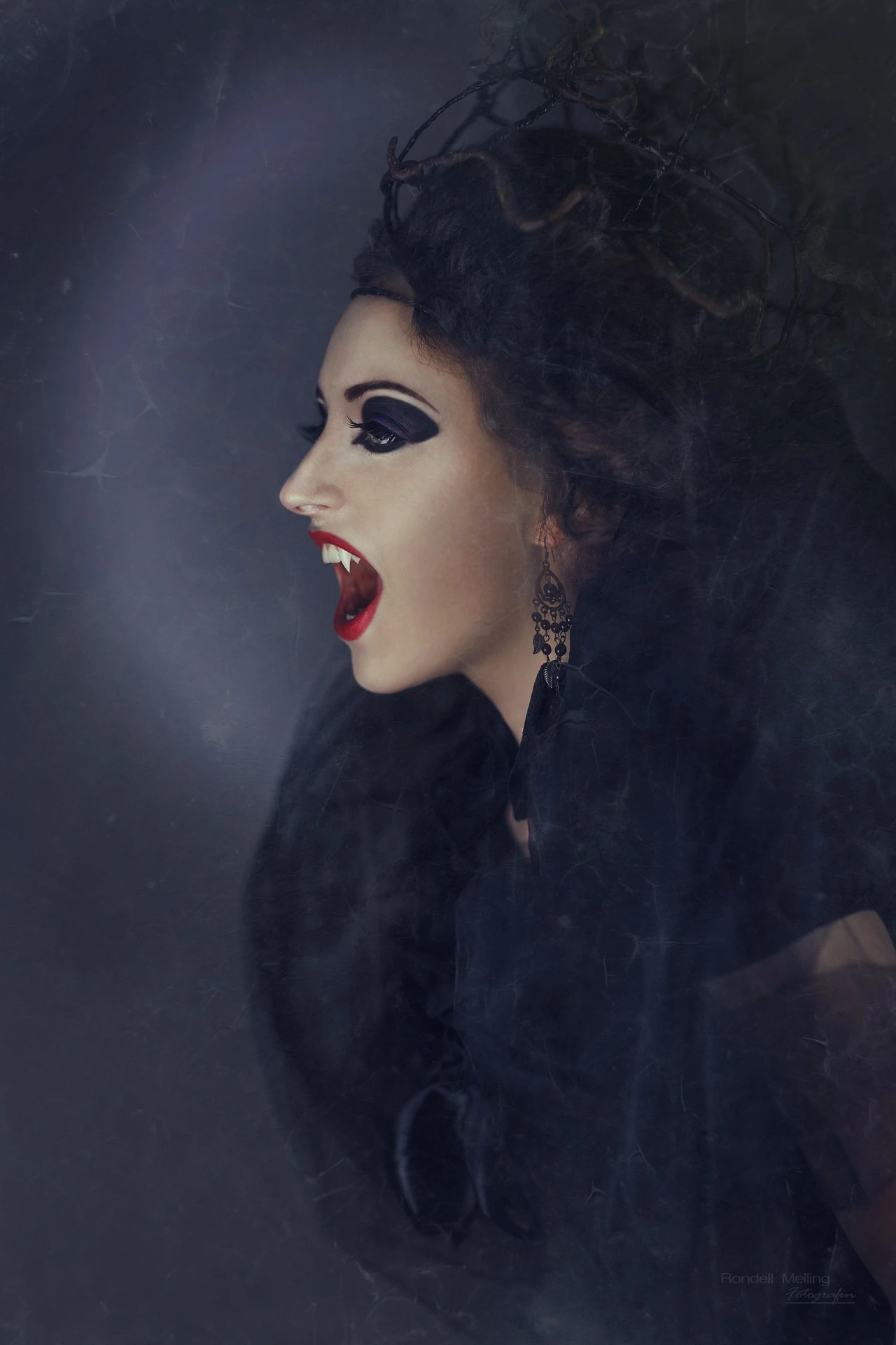 Close-up of a gothic woman with dramatic dark makeup, bared fangs, and an intense, vampiric expression.