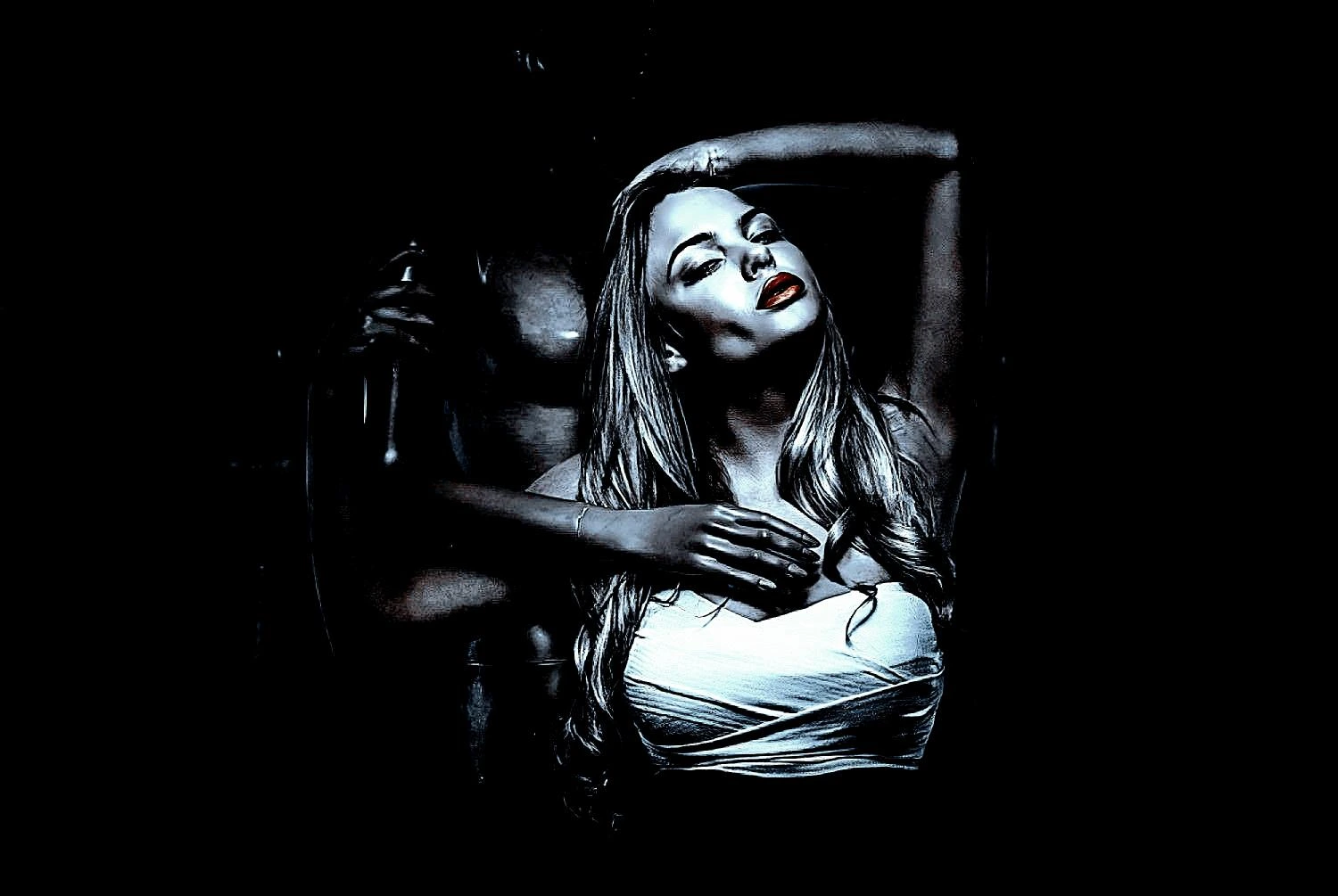 Portrait of a blonde woman leaning against a muscular figure, her striking red lips contrasting against the dark background.