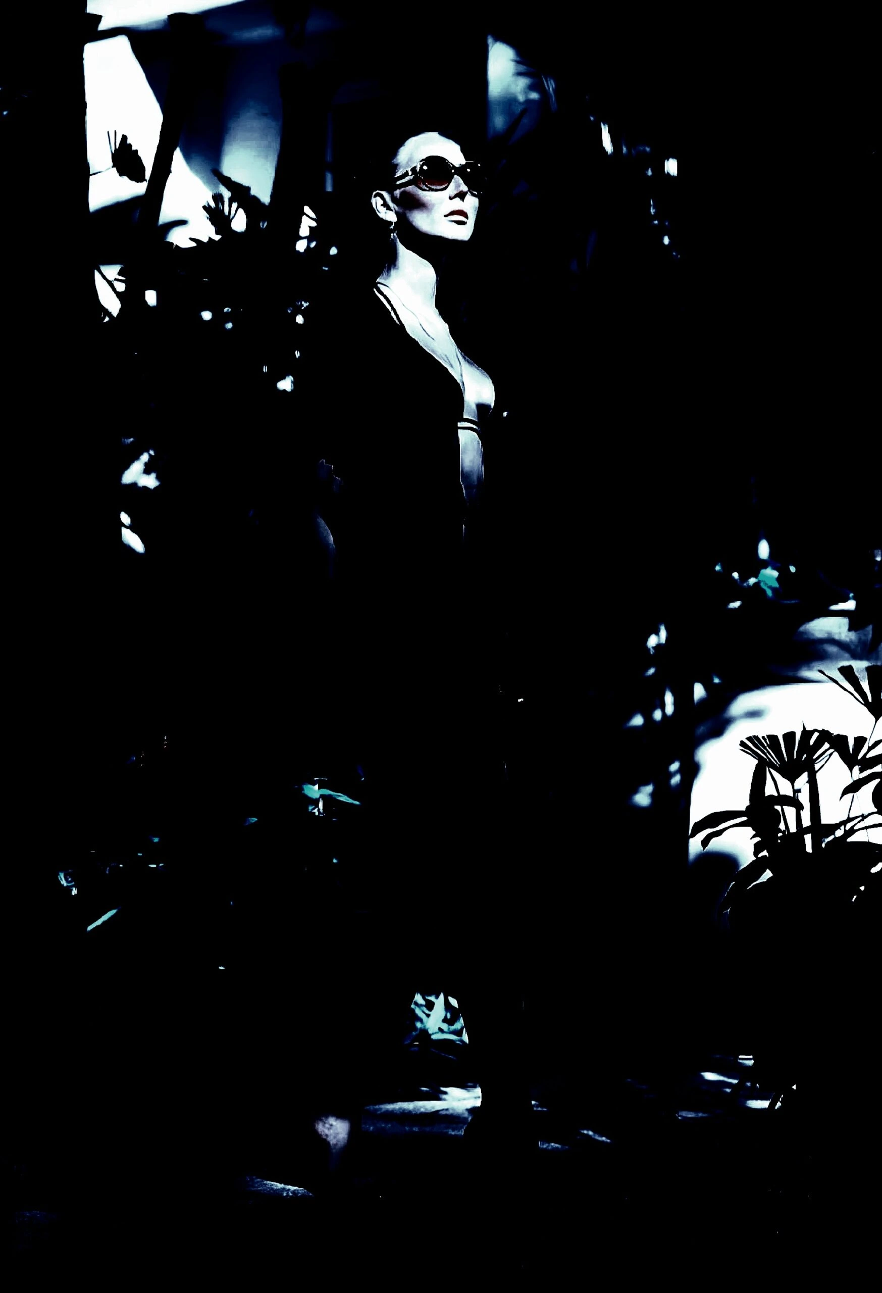 Stylish woman in sunglasses and a black dress, standing in a dark, atmospheric setting.