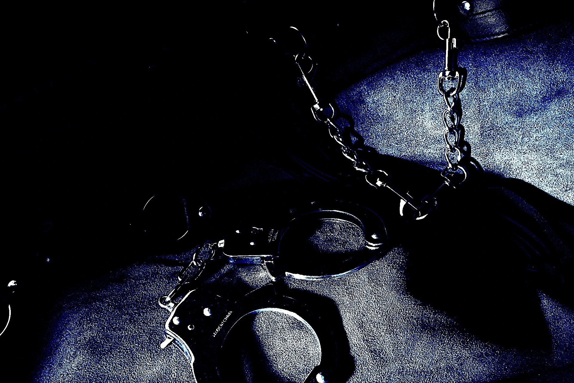 Metal handcuffs and chains laid on a dark leather surface, evoking a sense of restraint and control.