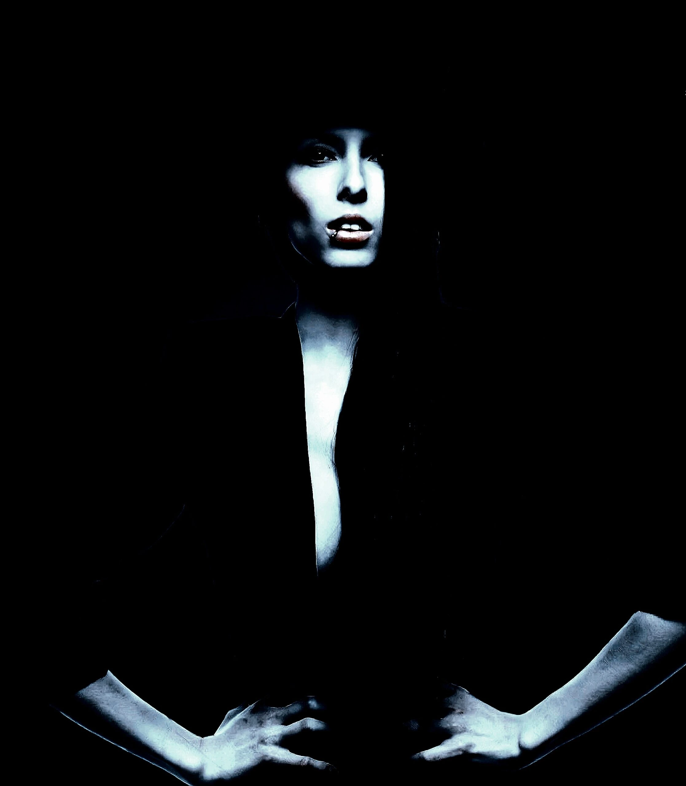 A woman with a piercing stare, hands on her hips, partially hidden in shadows, exuding confidence and intensity.