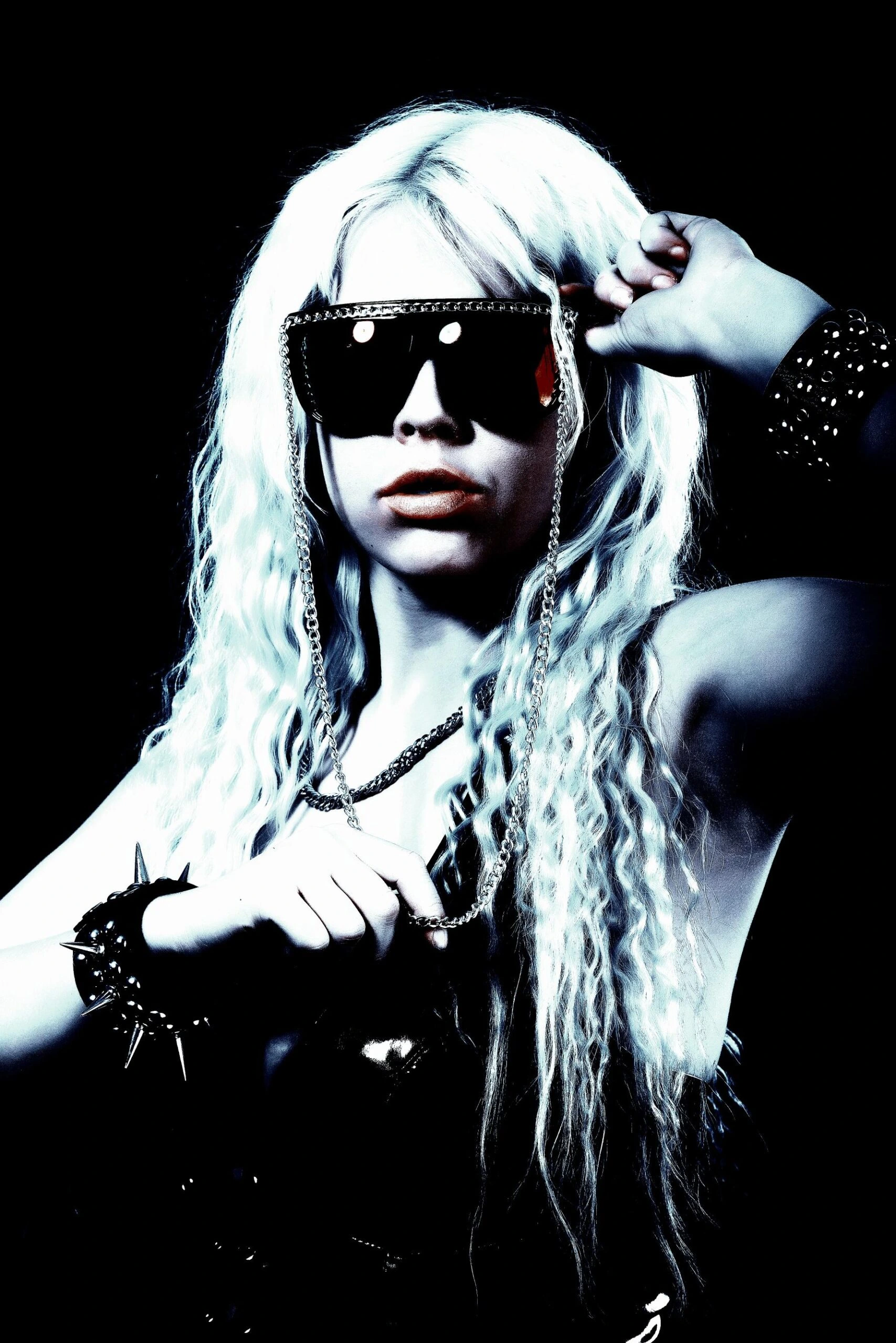 Woman with platinum blonde hair and oversized chain sunglasses, flaunting punk rock style and attitude."