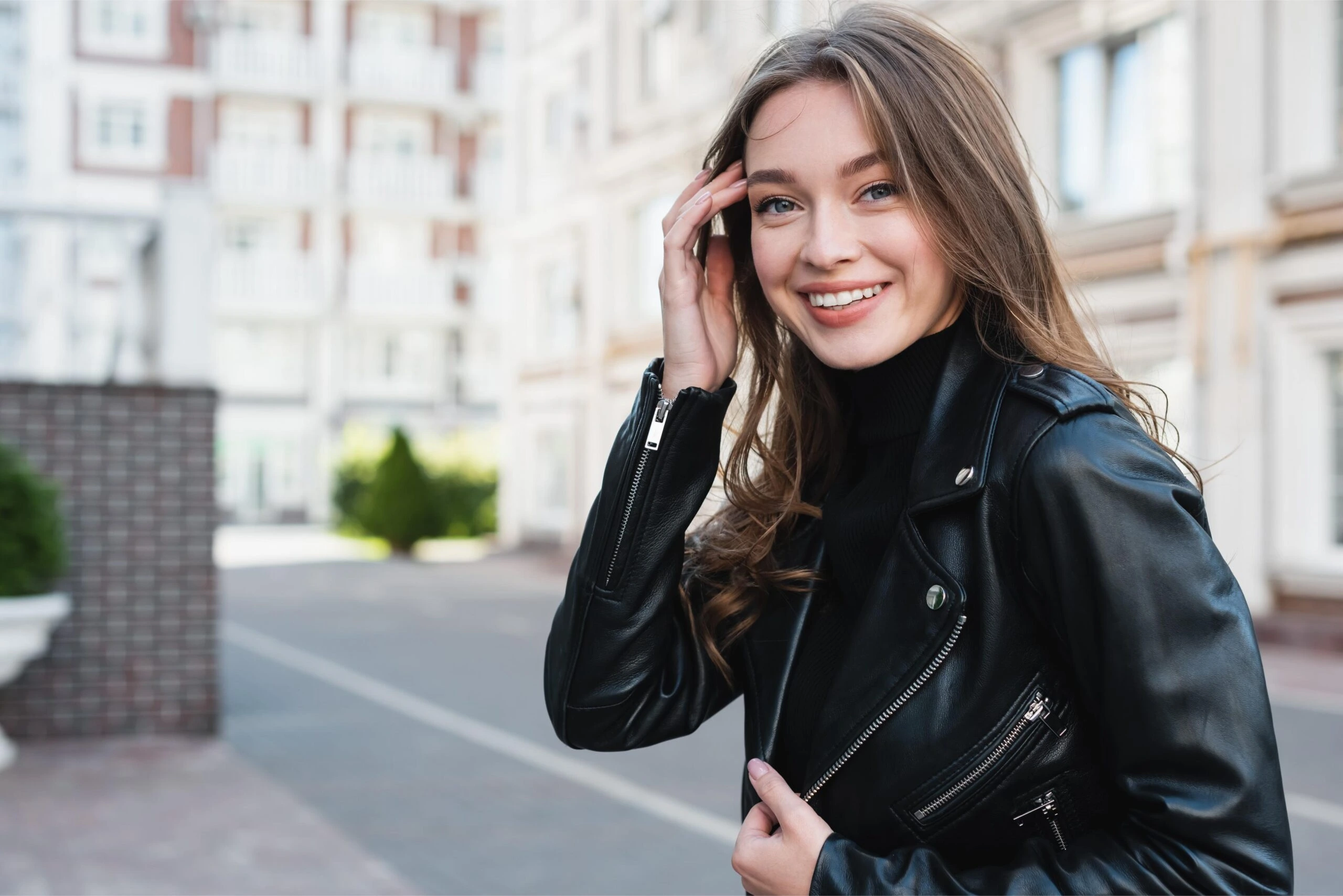 Woman in a sleek black leather jacket smiling outdoors, embodying casual goth-inspired fashion.