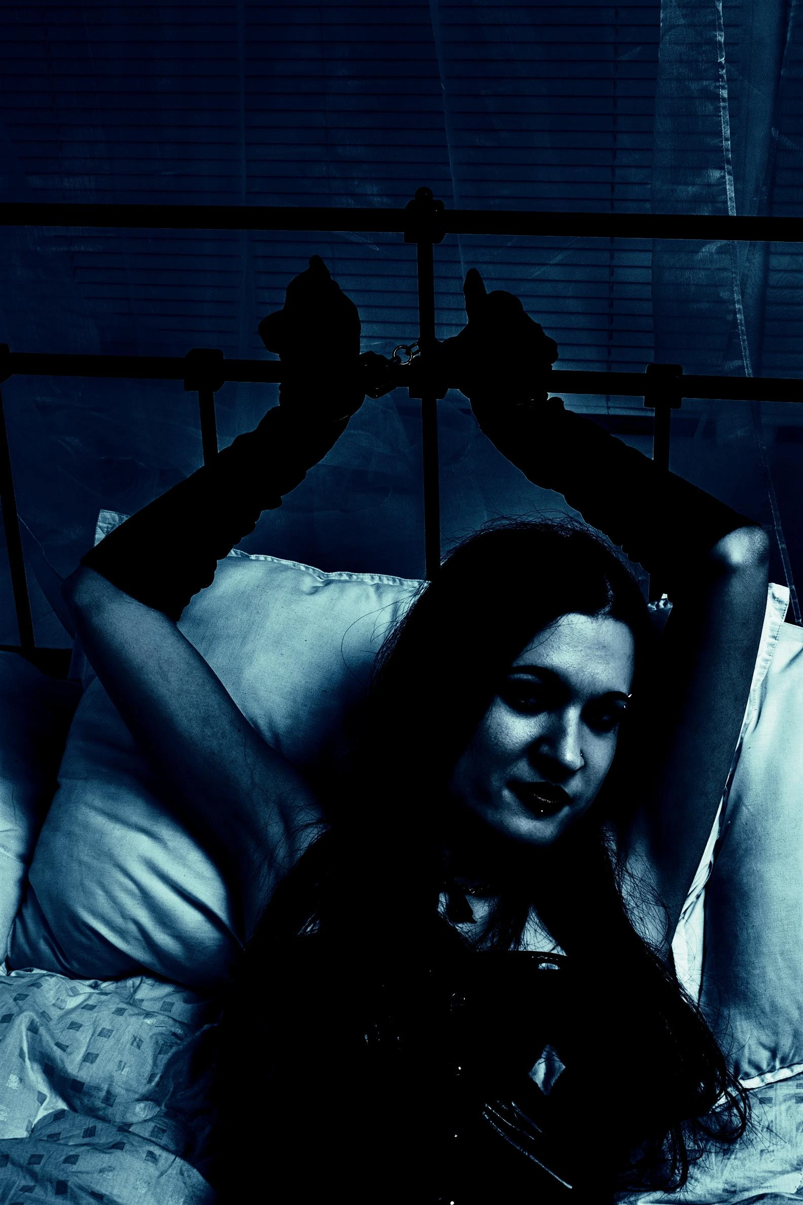 Dark-toned silhouette of a woman in handcuffs, lying on a bed with a mysterious, gothic atmosphere.