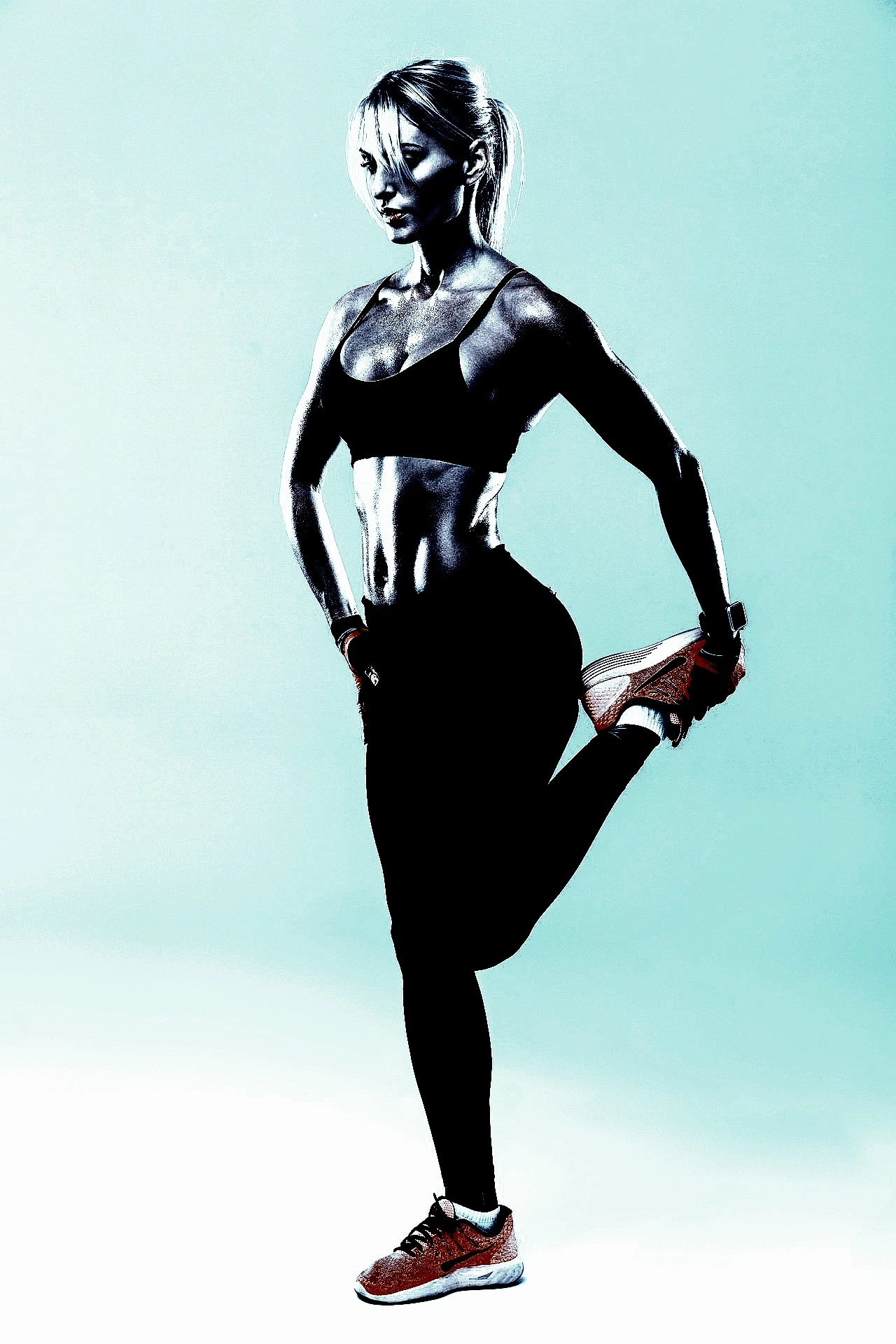 Athletic woman stretching her leg in a well-lit studio, showcasing her toned physique and dedication to fitness.