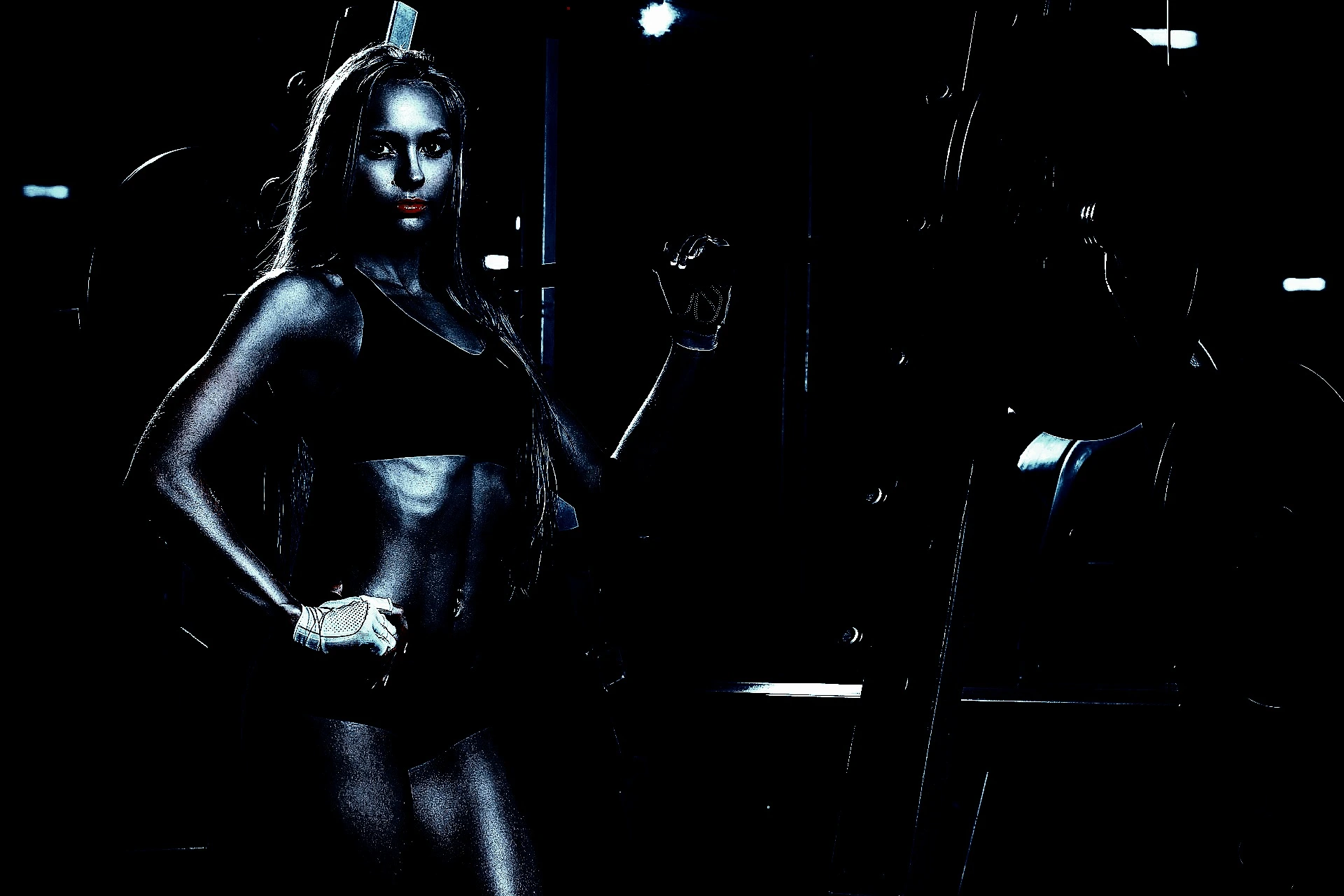 Strong woman in a black sports outfit posing in a dimly lit gym, exuding power and gothic energy.