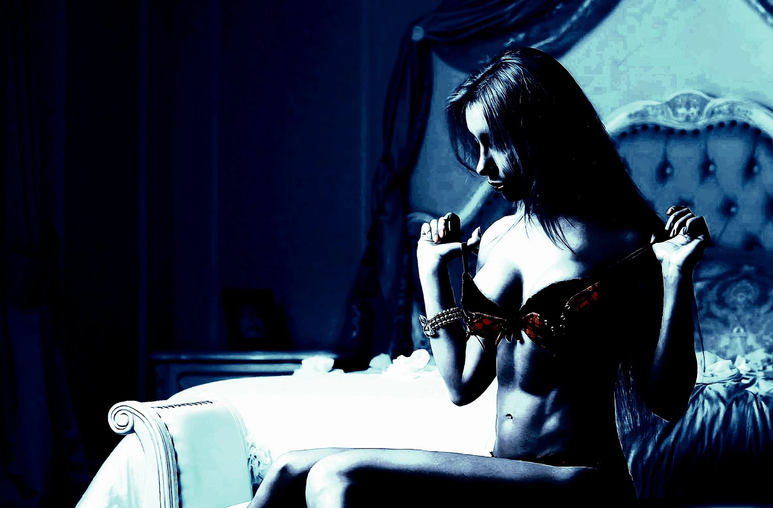 Woman in a black bra sitting on a luxurious bed, pulling her lingerie strap in a provocative, low-light ambiance.