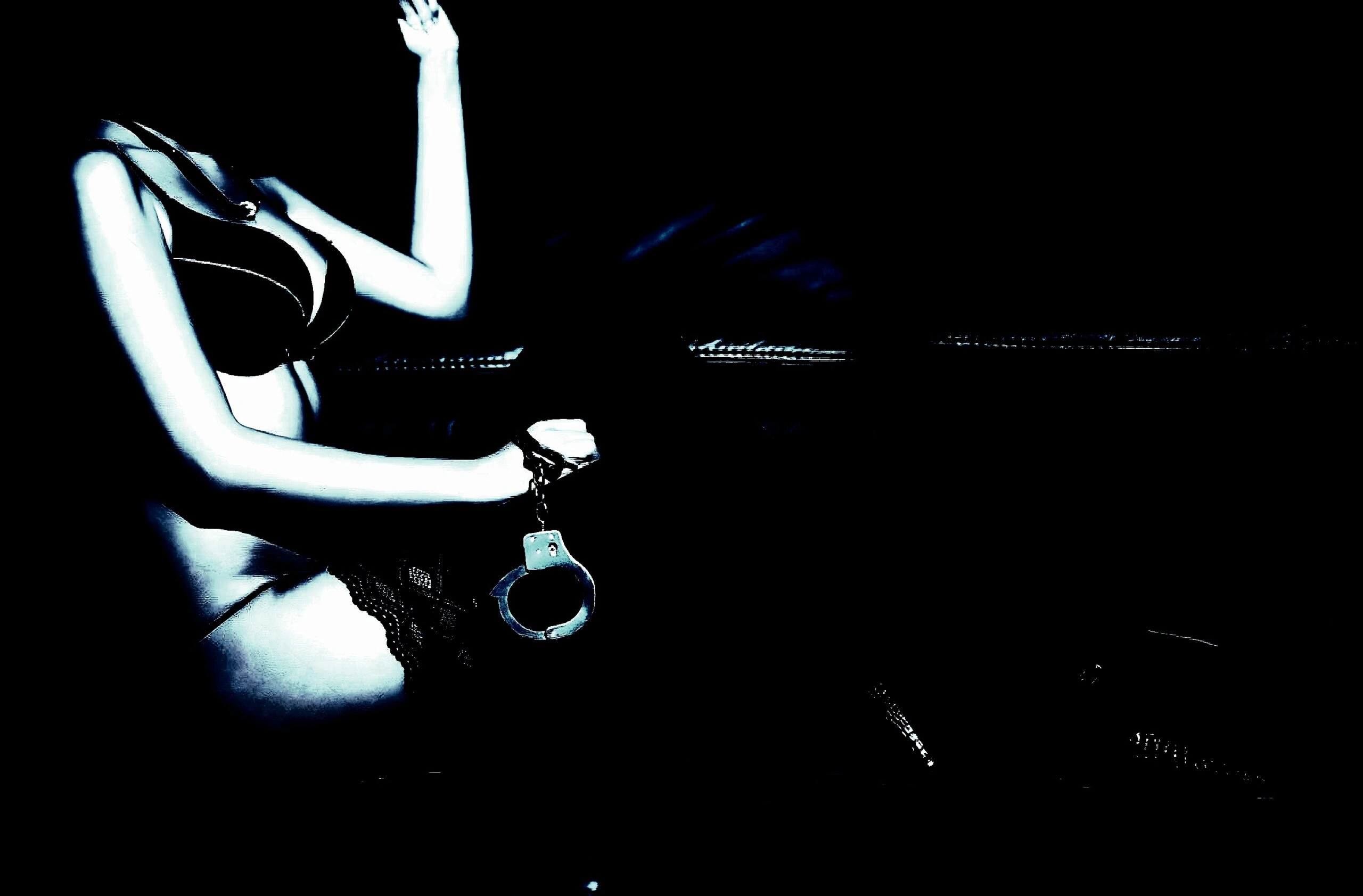 Woman in lingerie holding handcuffs, silhouetted dramatically against a dark background.
