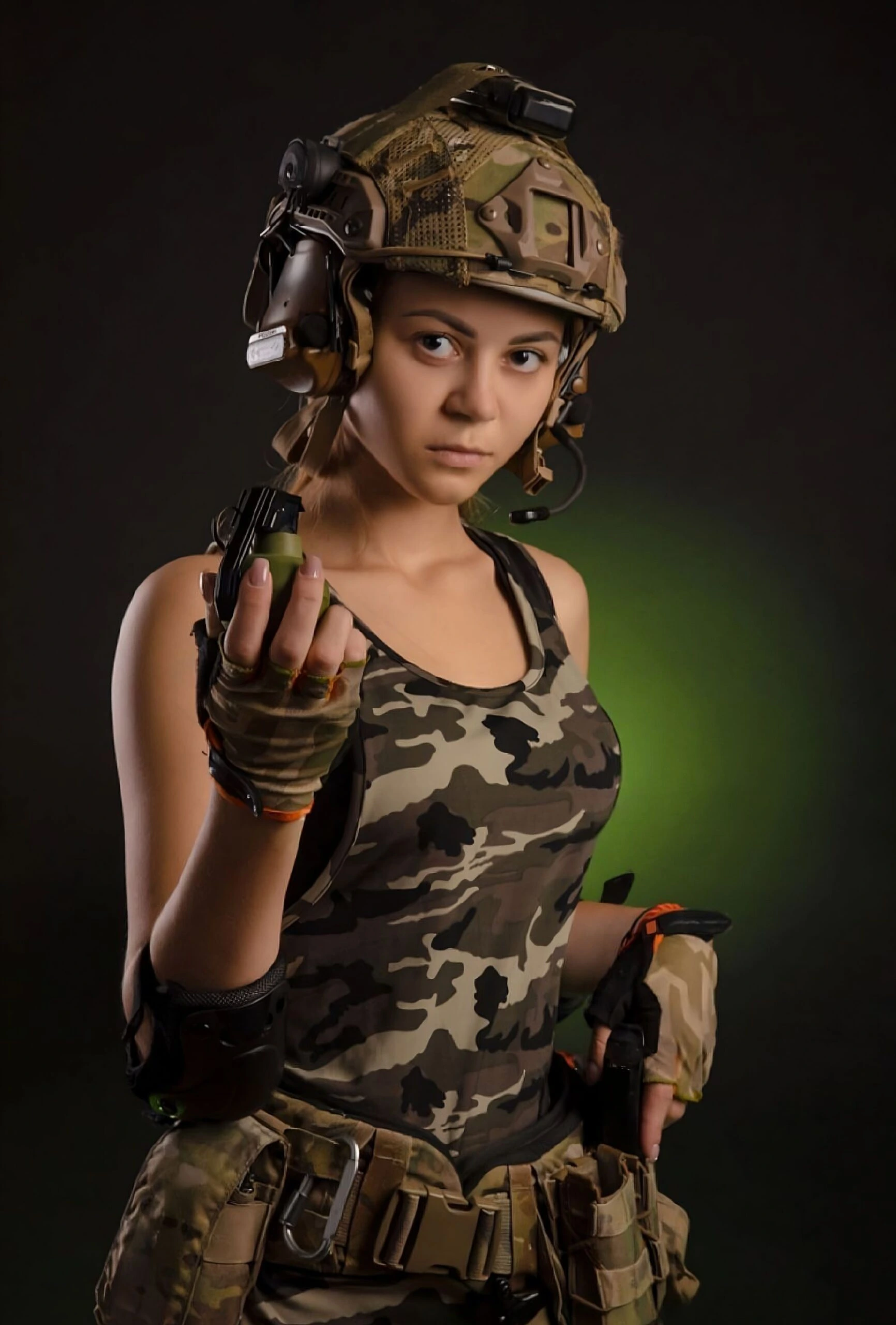 A determined woman in military gear, wearing a camo helmet and gloves, holding a grenade with a serious expression against a dark green-lit background.