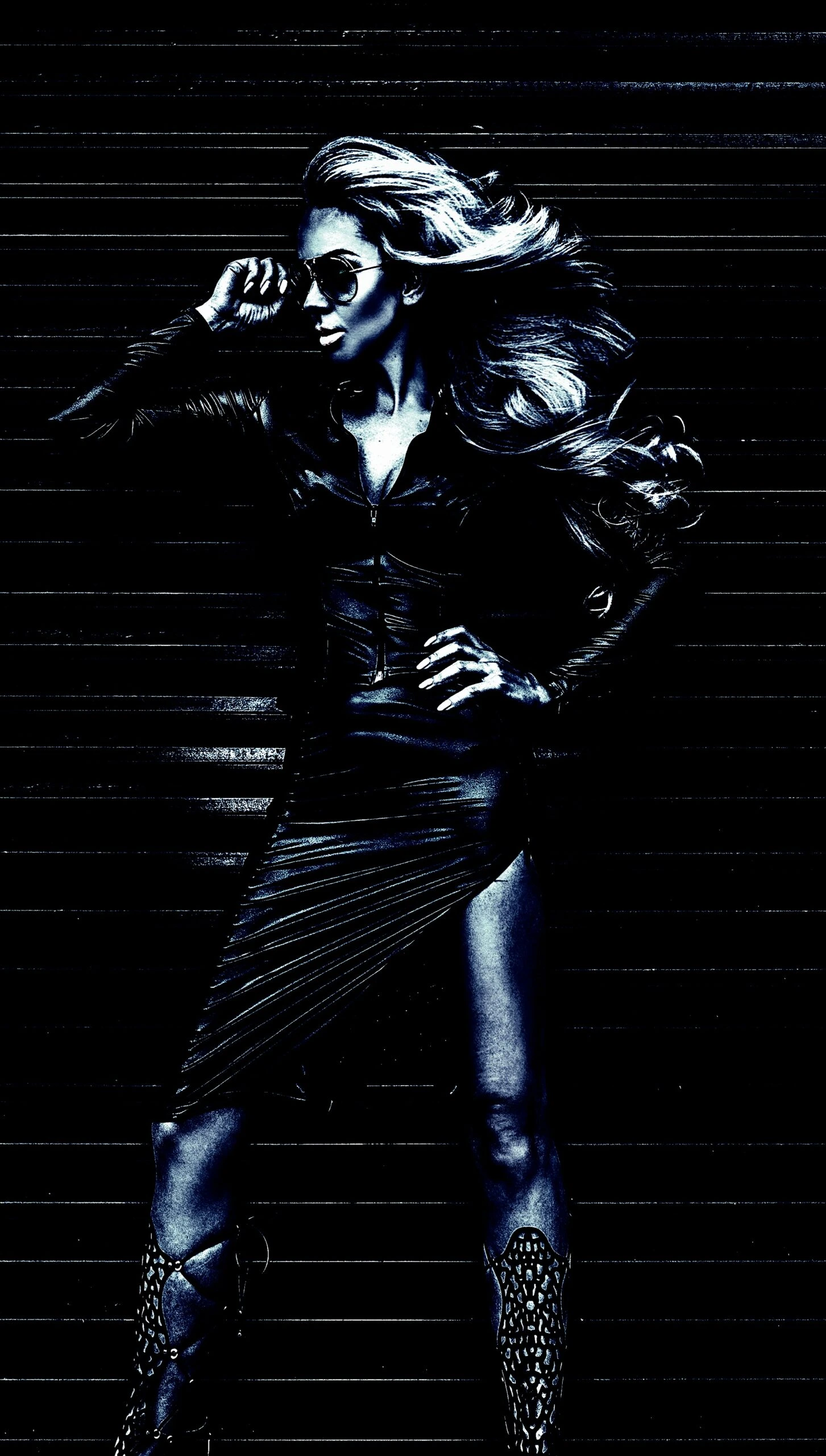 A fierce woman in a leather outfit with wind-blown hair, posing confidently against a dark, industrial backdrop.