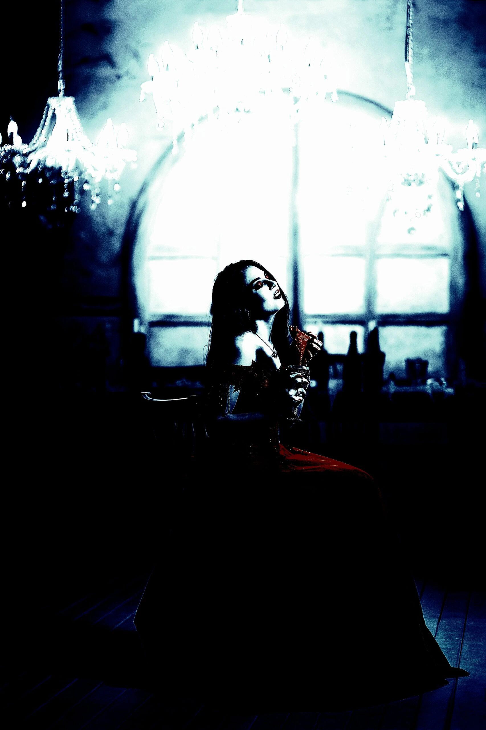 A hauntingly beautiful woman seated under crystal chandeliers, wearing a gothic gown in a dimly lit room.