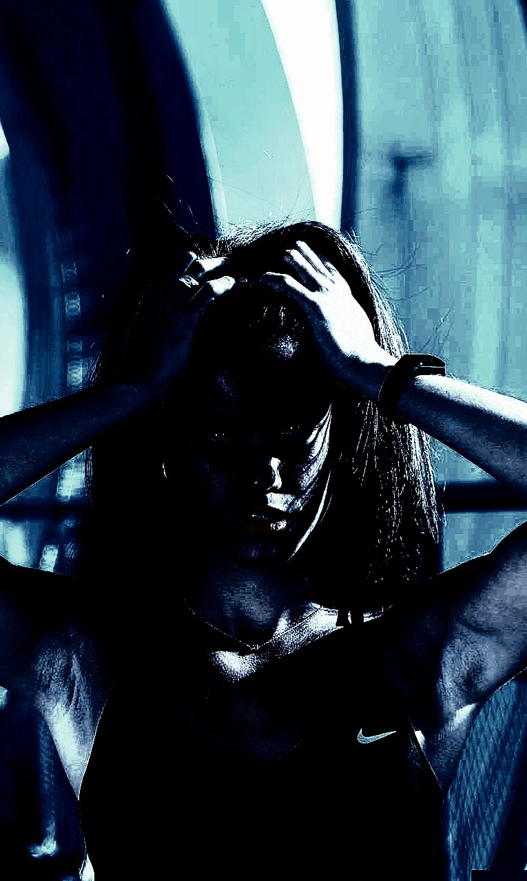 Shadowy woman with intense expression, holding her head with both hands, in dramatic blue lighting during a workout.