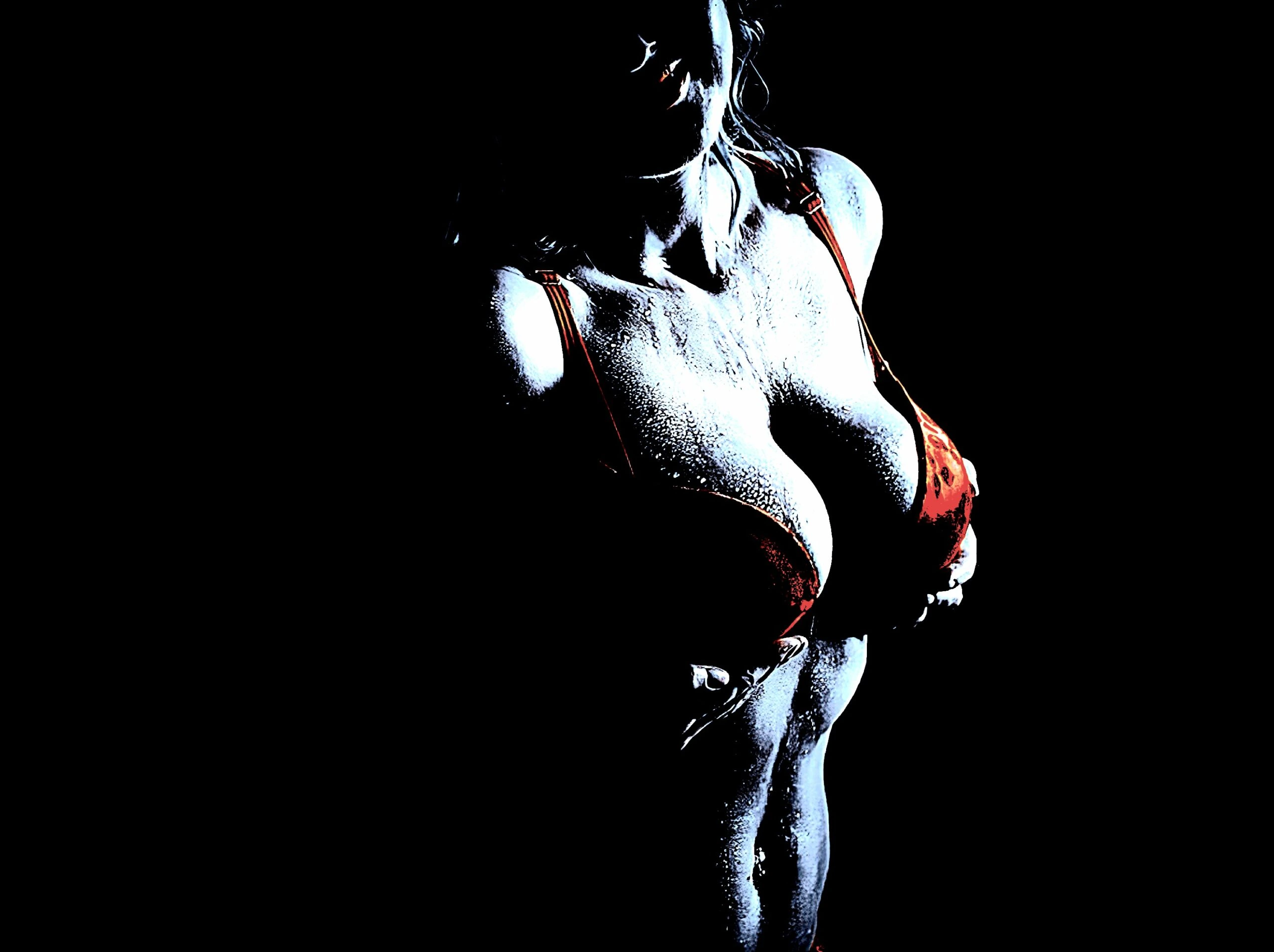 A close-up of a woman in a red bra, her torso glistening under dramatic lighting.