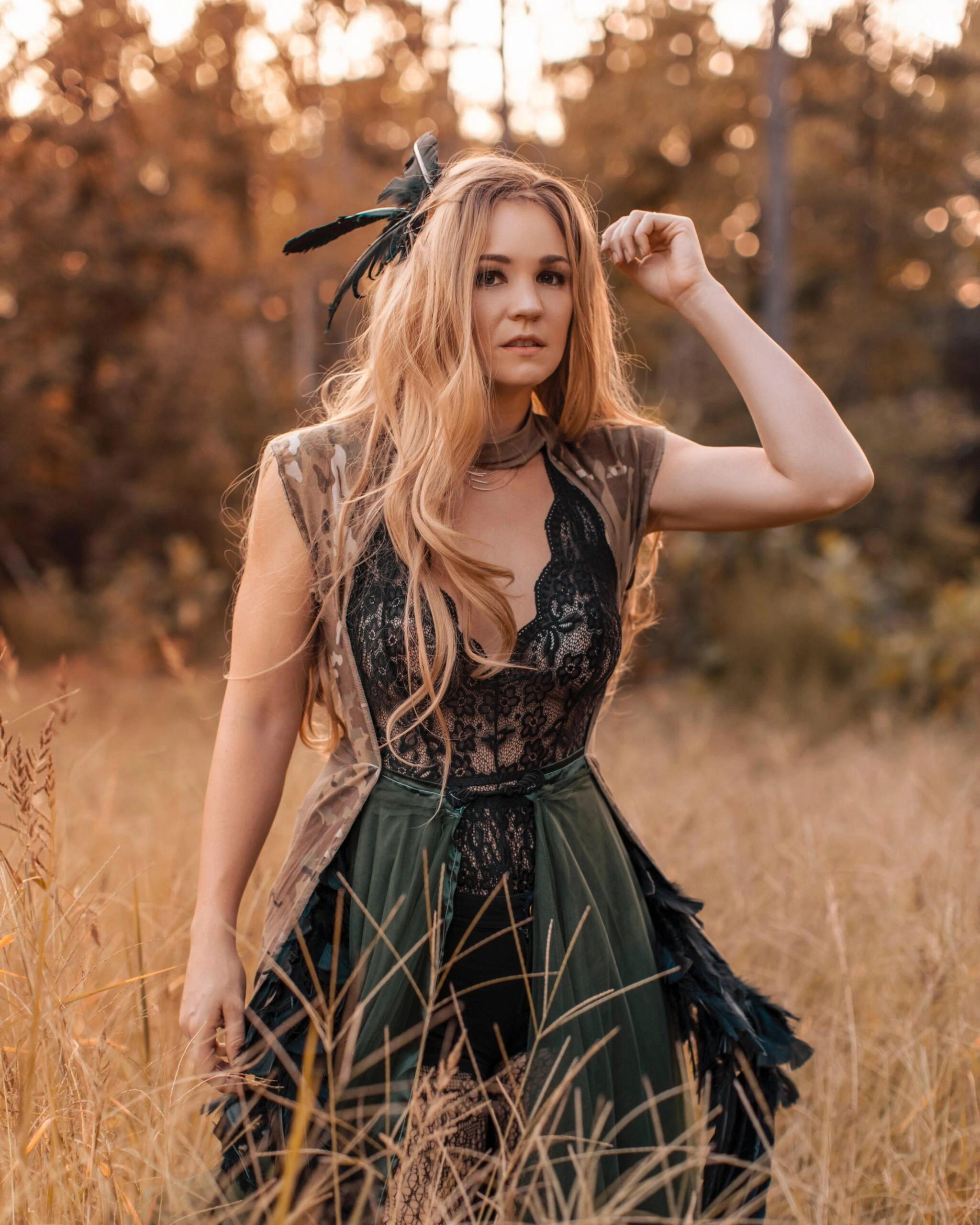 A woman in a fantasy-inspired gothic outfit, wearing a green and black lace dress with feathered accessories in a forest setting.