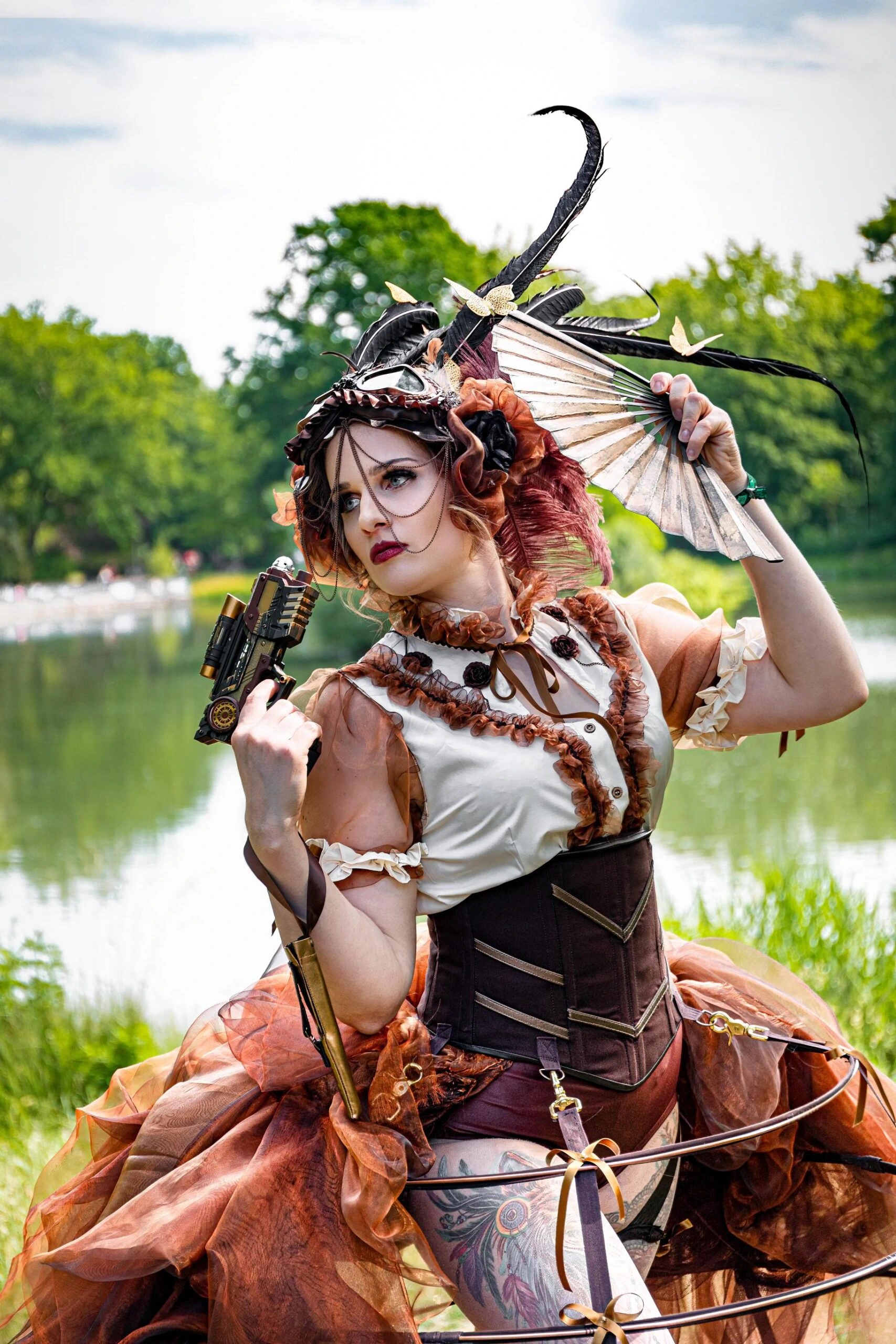 A steampunk-inspired woman in an elaborate outfit with a corset, lace details, and mechanical accessories, holding a fan and a prop gun outdoors.