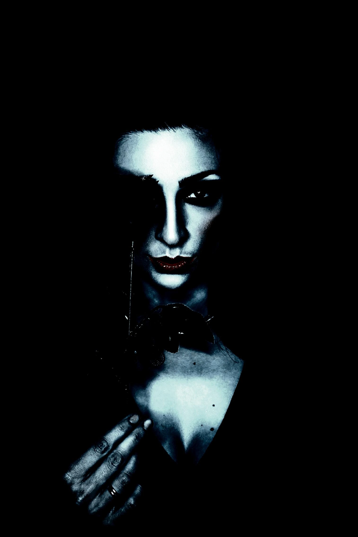 A gothic woman with dramatic lighting, dark lipstick, and intense gaze, holding a feather against her face in a mysterious pose.