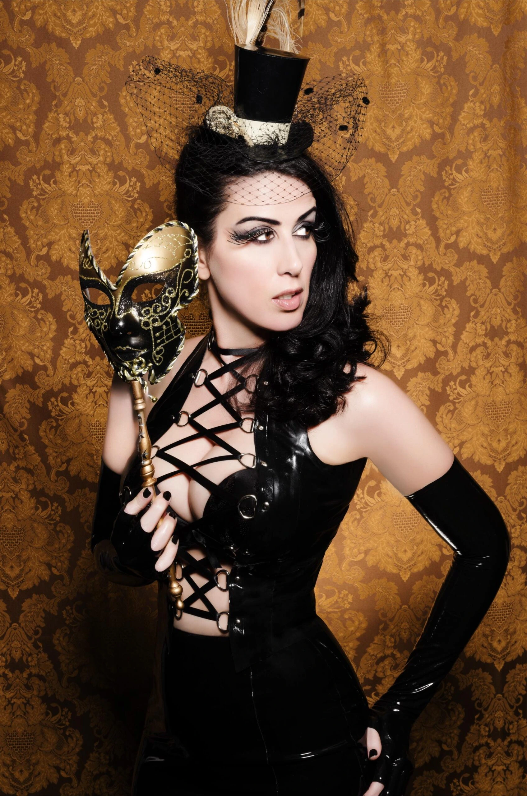 Gothic woman in a black latex corset with intricate lace-up details, accessorized with a masquerade mask and feathered top hat against a golden ornate backdrop.