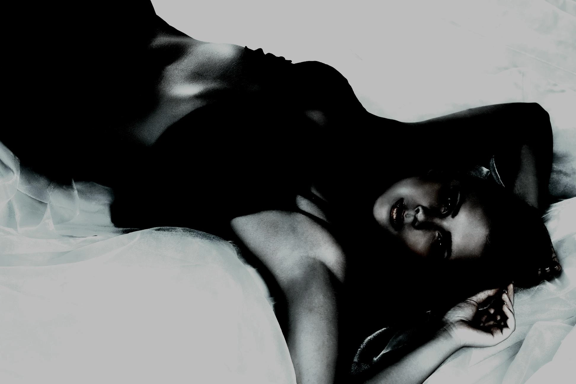 Sensual woman in a dark outfit, reclining on soft fabric with a seductive, captivating stare.