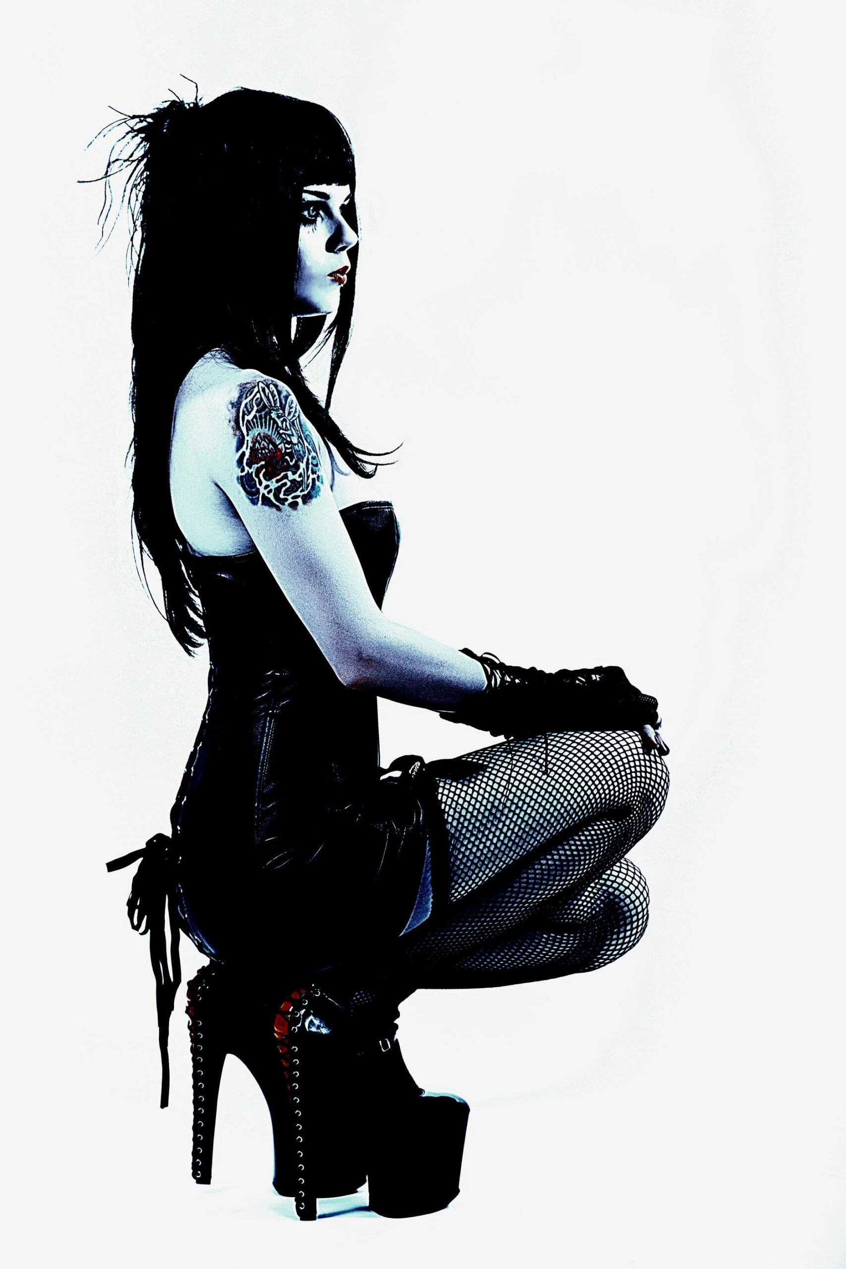 Profile of a gothic model wearing a patent leather corset and fishnet stockings, seated in platform heels with a moody expression.