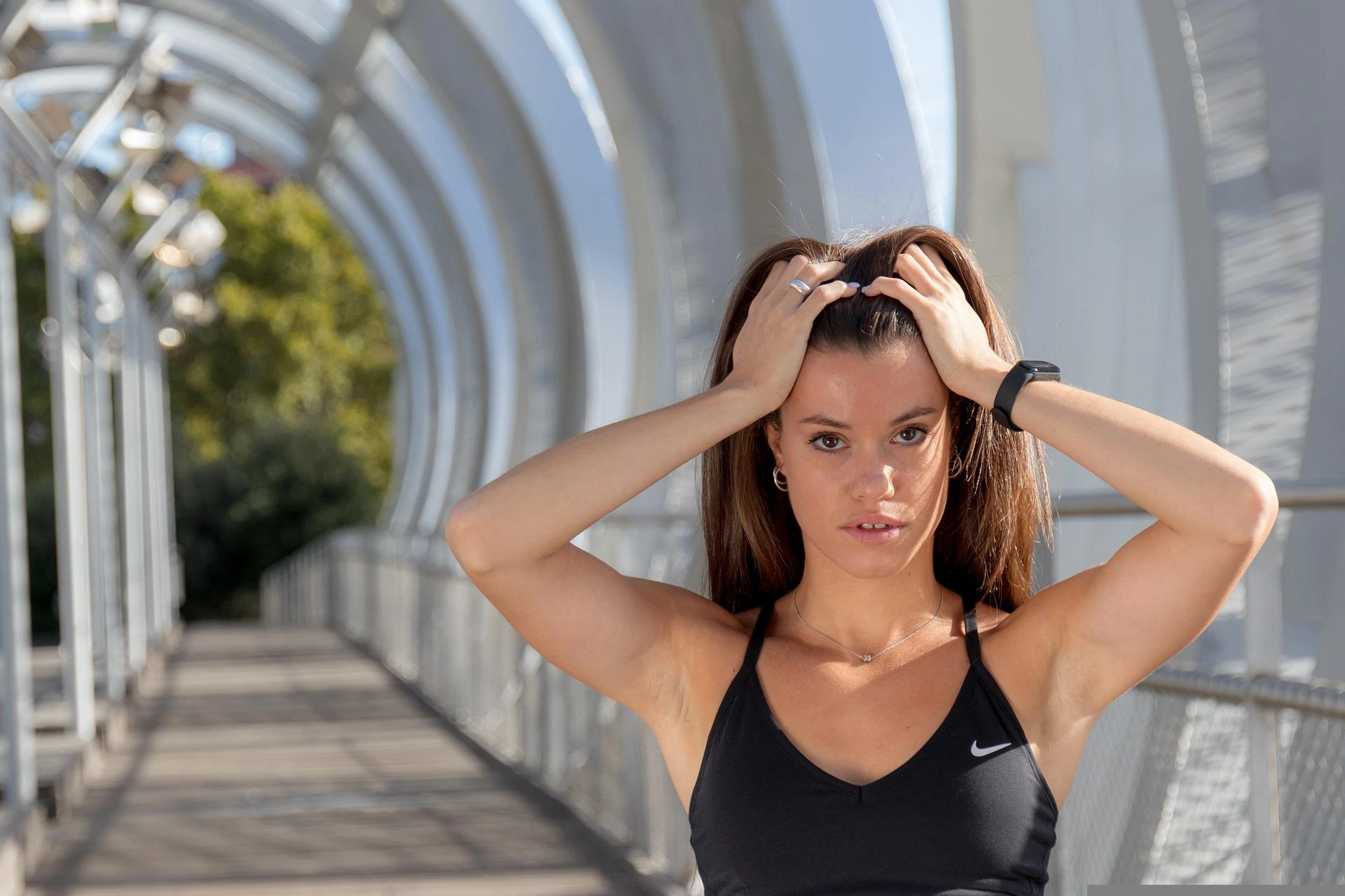 Focused athletic woman in a black sports bra standing on a futuristic bridge, preparing for an intense workout.
