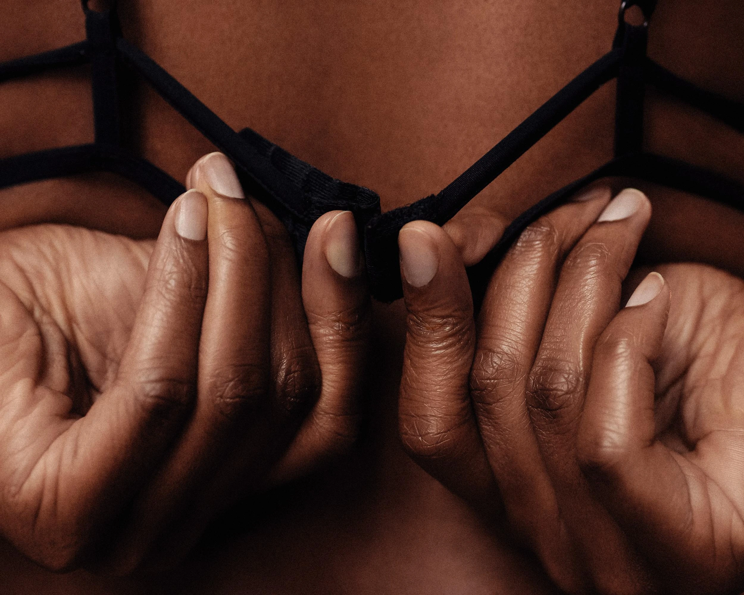 Hands fastening a black strappy bra, emphasizing the delicate and gothic-inspired design of the lingerie.