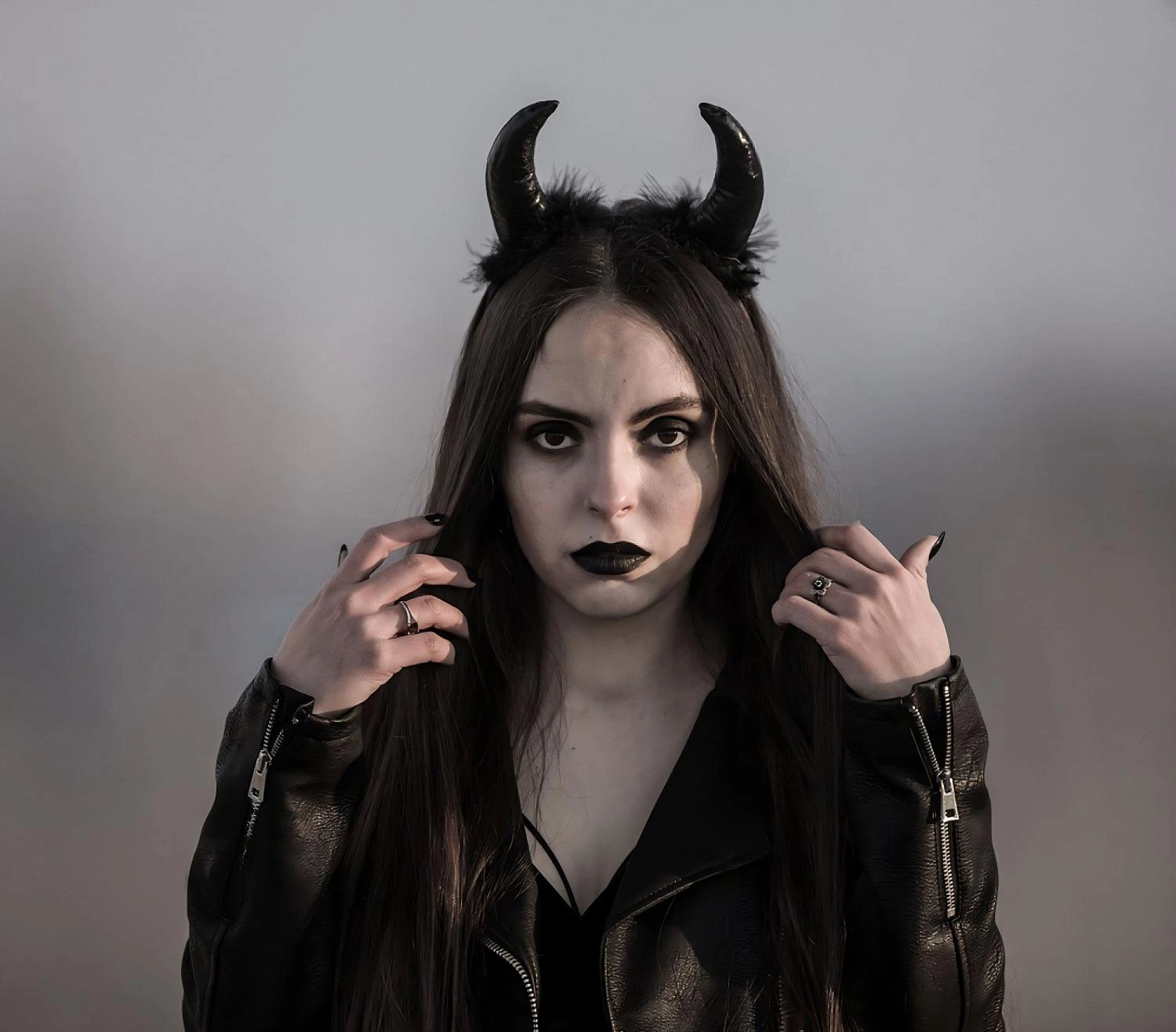 Gothic woman with devil horns, black lipstick, and leather jacket in moody lighting