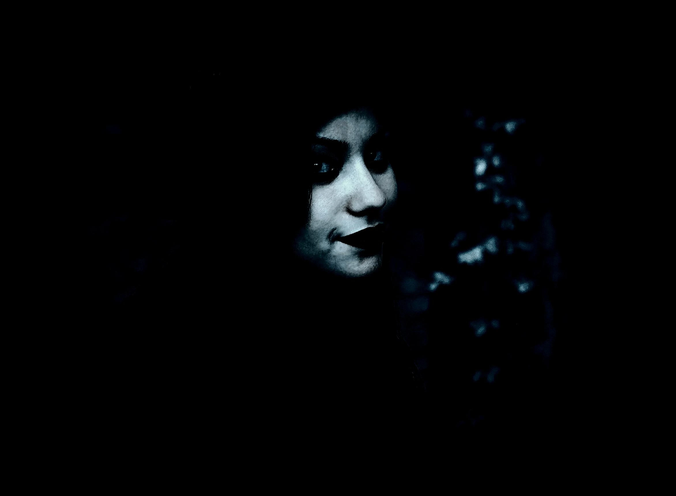 Mysterious woman with dark lipstick smirking in shadows, barely illuminated by soft light