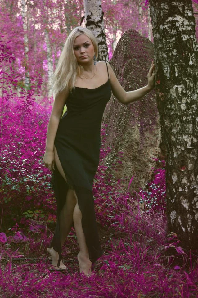 Blonde woman wearing high heels and black slit dress in surreal pink-toned forest
