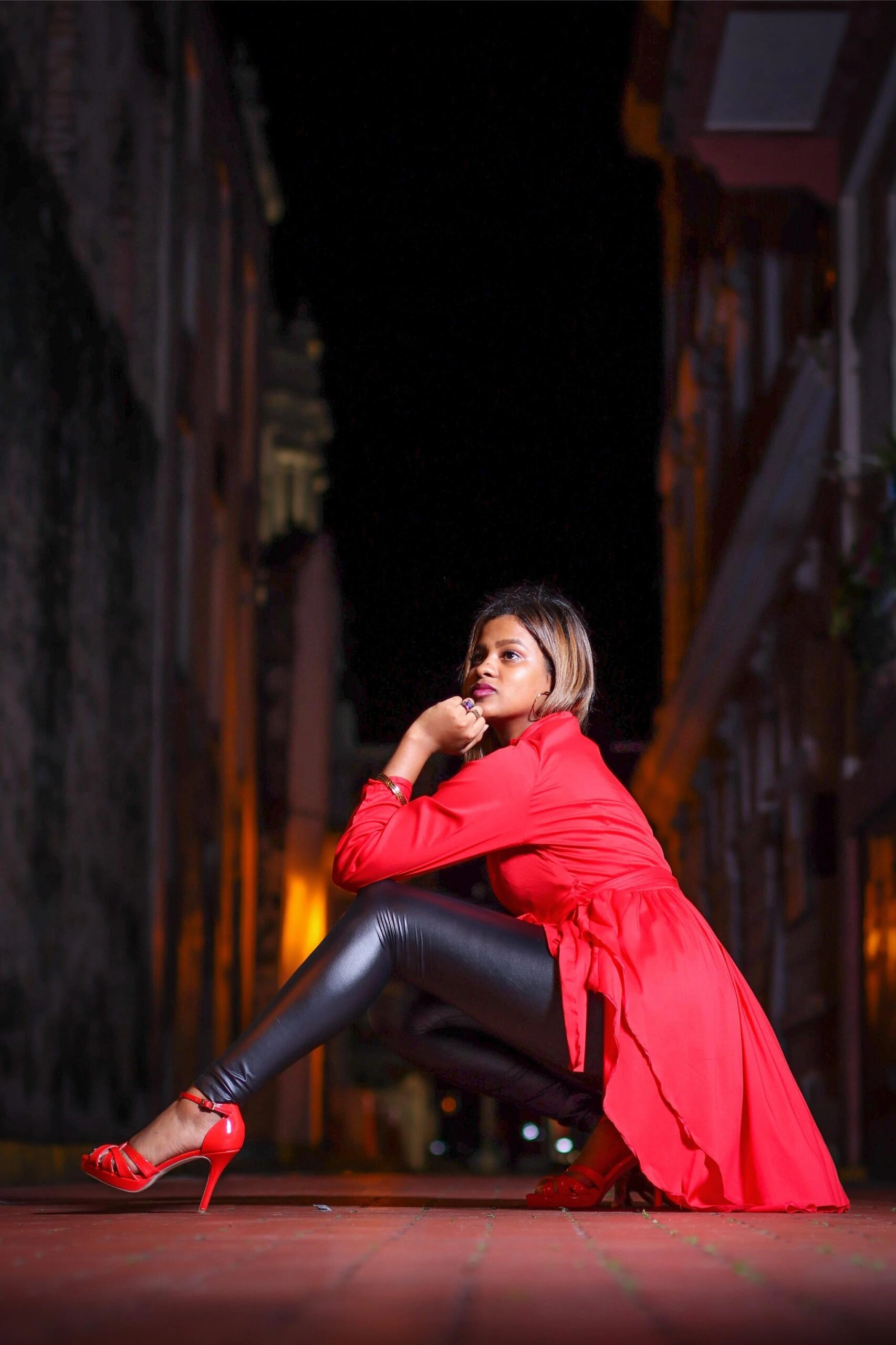 Woman in red trench coat and red high heels crouching on street at night