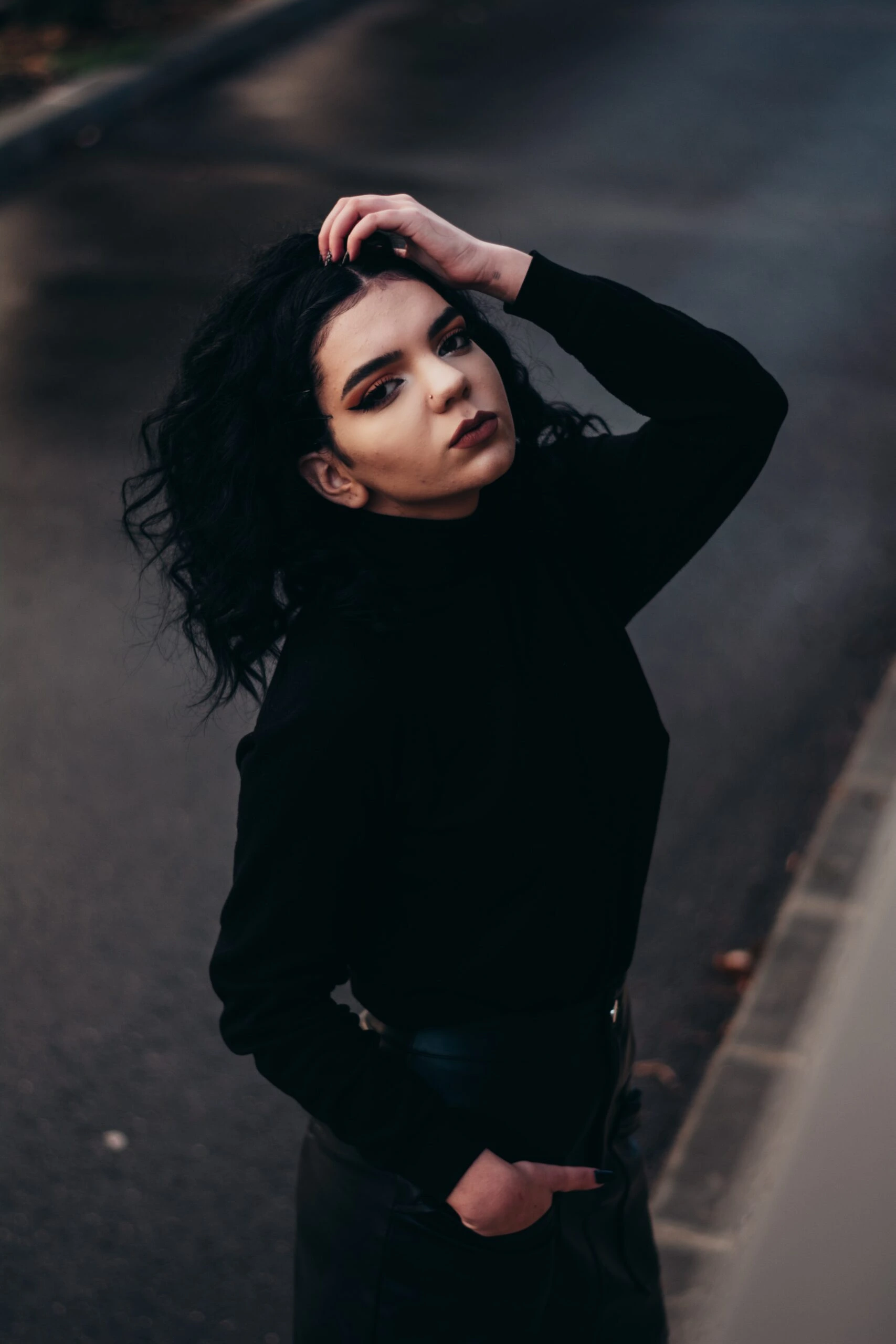 Gothic woman in black turtleneck with bold makeup posing outdoors with hand in hair