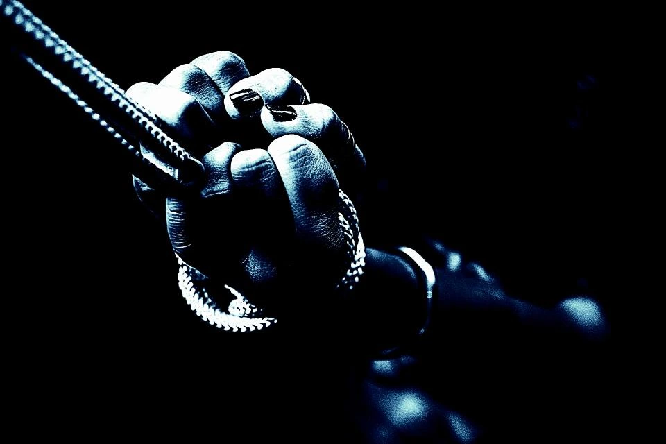 Close-up of a hand tightly gripping a braided rope in moody blue lighting 
