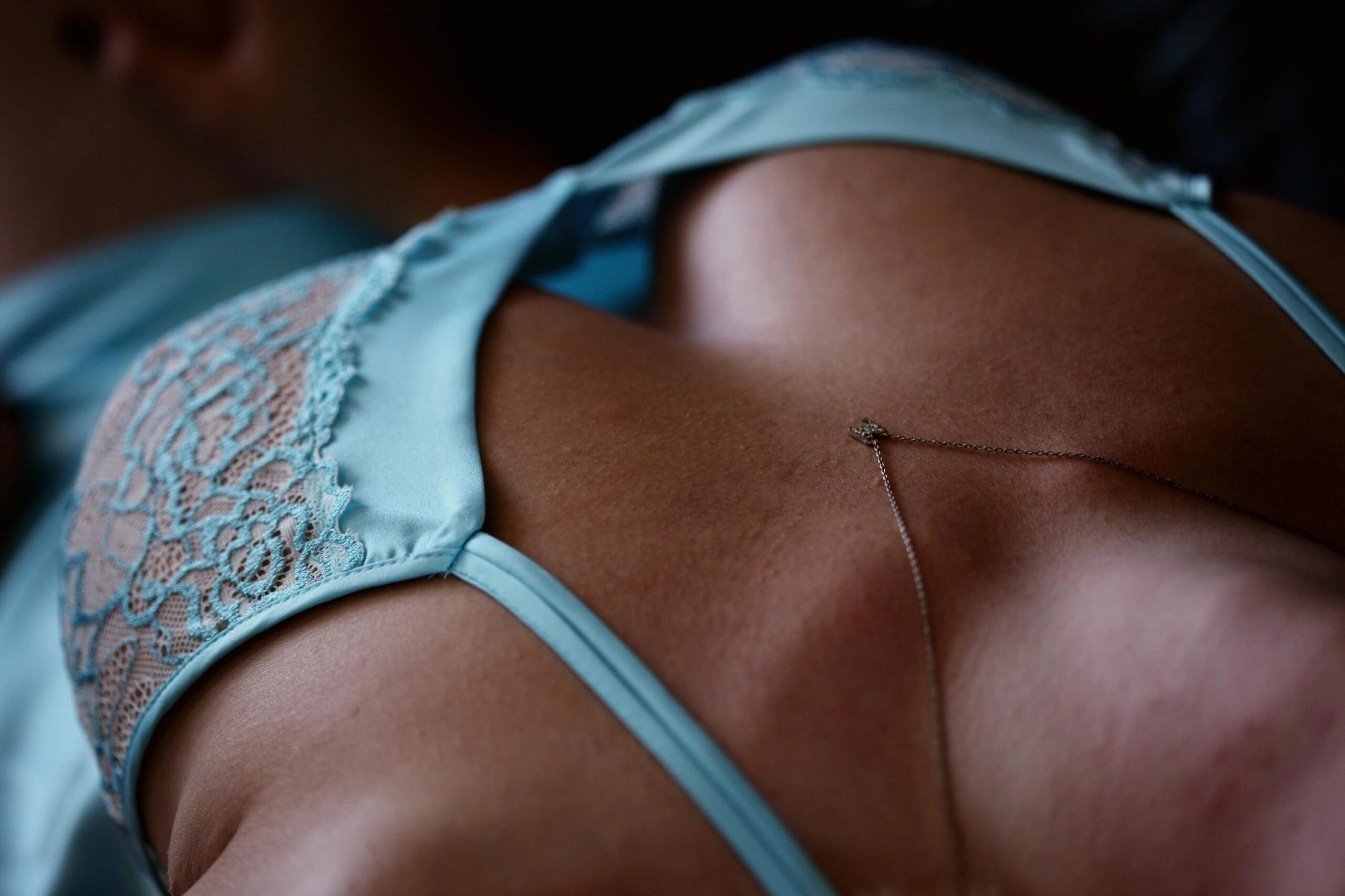 Close-up of a woman's back in light blue satin and lace lingerie, featuring a delicate chain accessory.